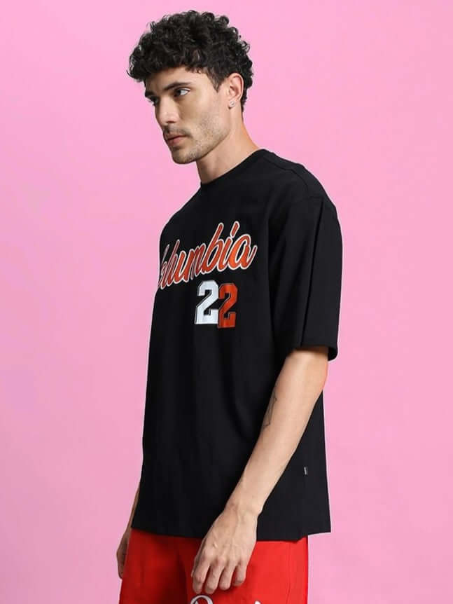 COLUMBIA 22 PRINT OVER-SIZED T-SHIRT BLACK modeled with urban street style on a pink background, highlighting the bold graphic design.