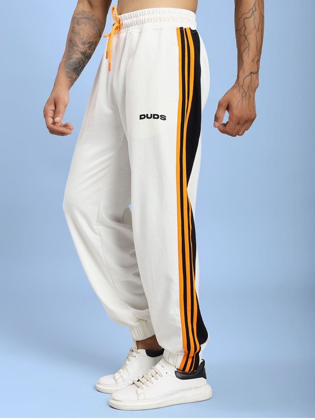 Person wearing COMFORT FLEX STRIPE JOGGER OFF-WHITE with black and orange stripe detail on blue background.
