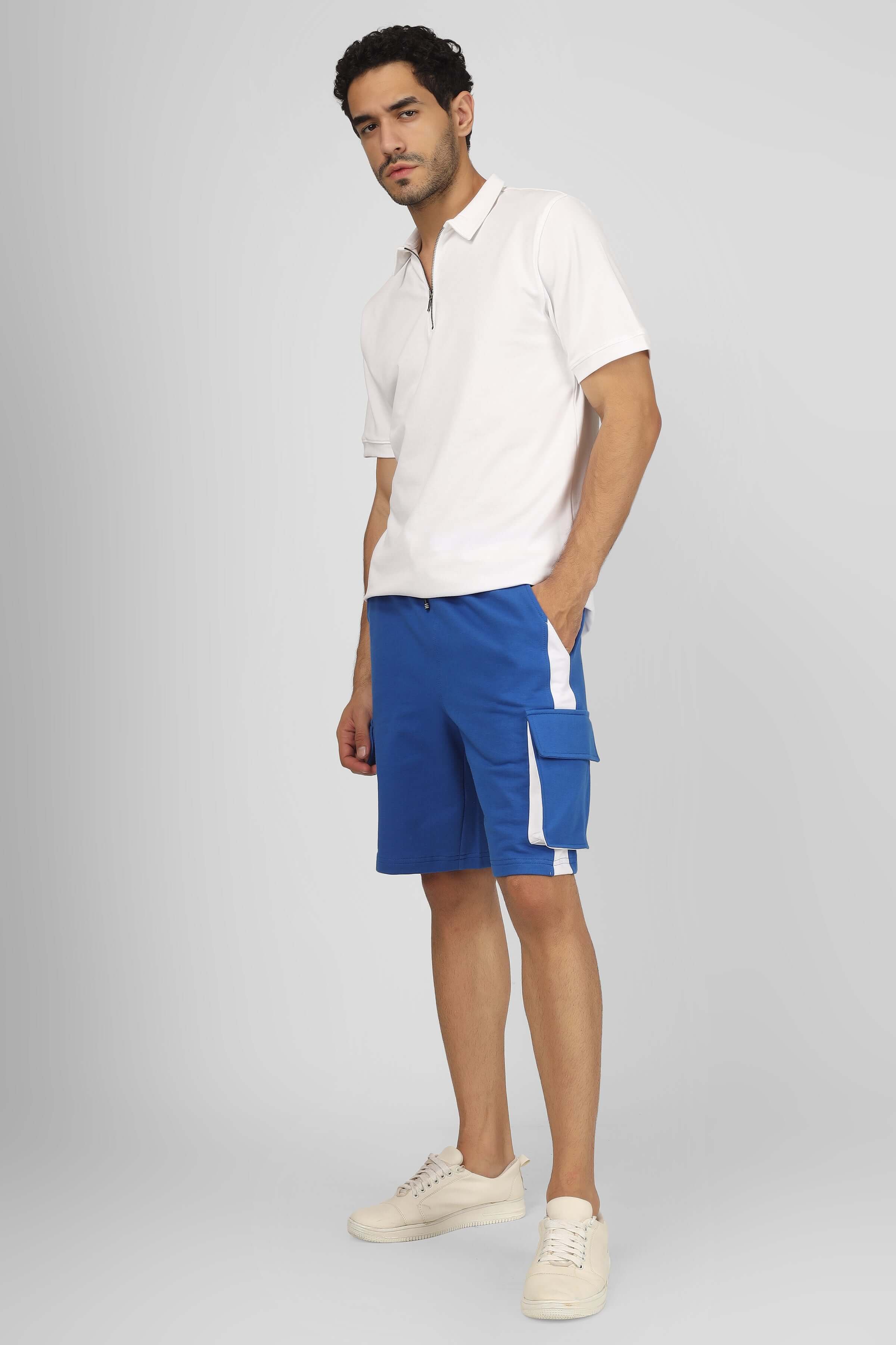 Model wearing CONTRA regular fit cargo shorts in royal blue and white paired with a white polo shirt and sneakers.