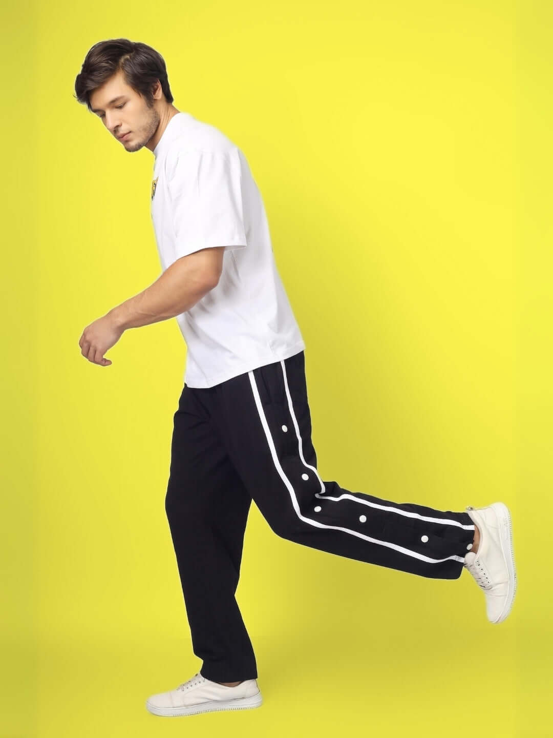 Man wearing black contrast panel joggers with white shirt, standing against a bright yellow background.