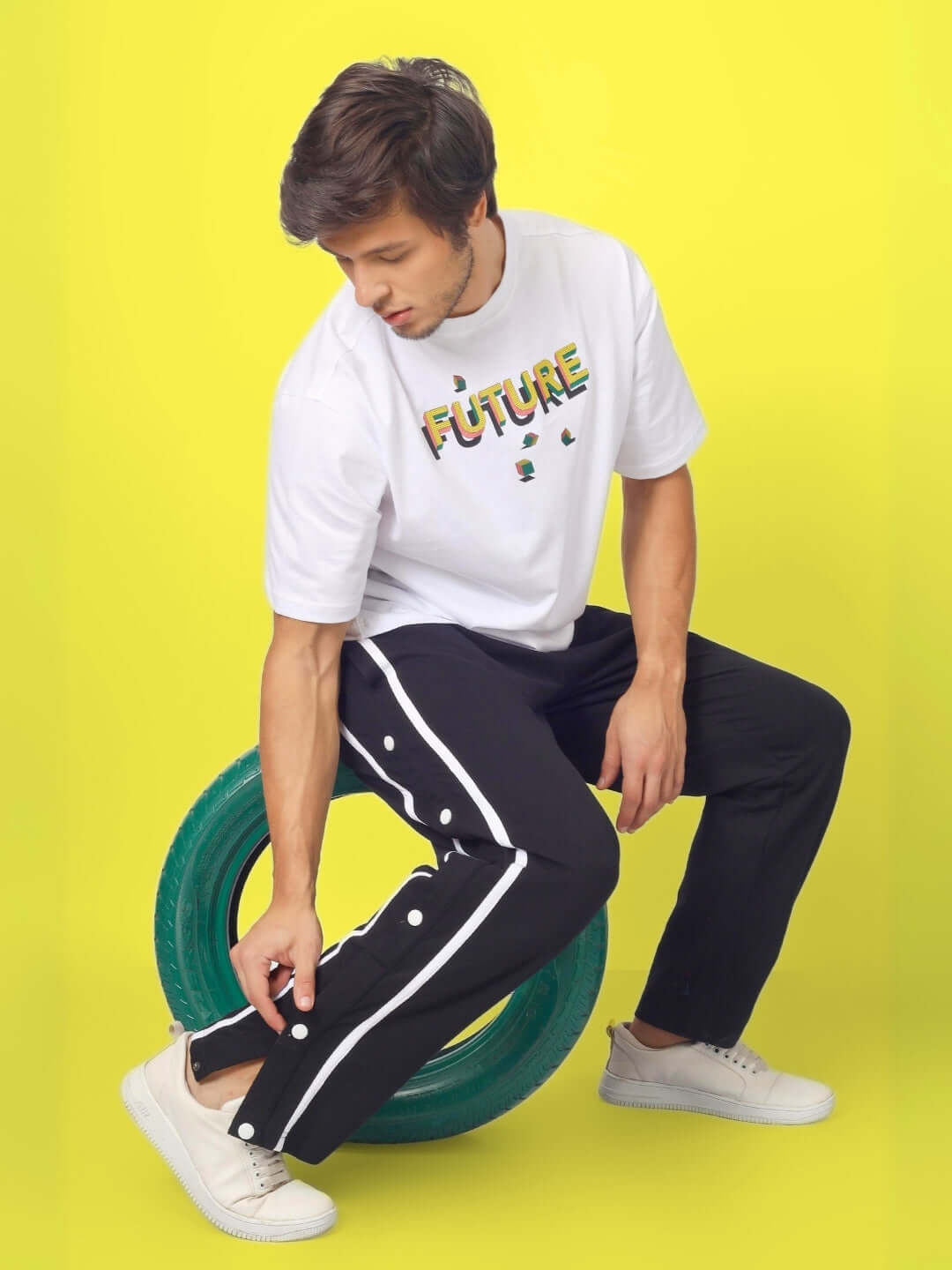 Model wearing black contrast panel joggers with white shirt, sitting on a tire against a yellow background.