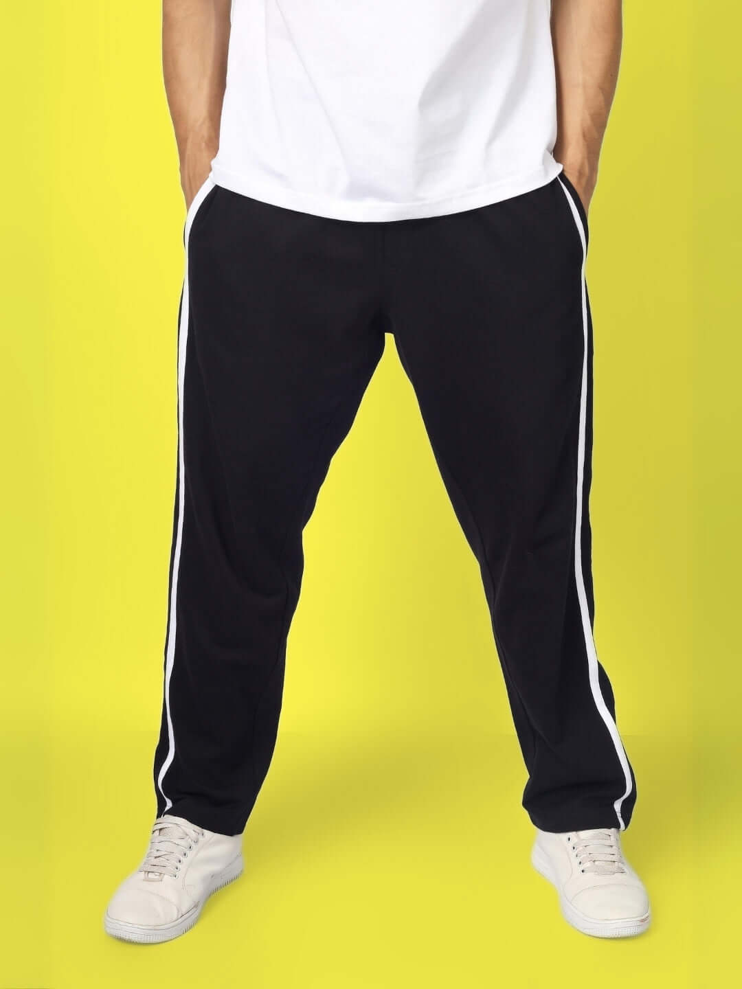 Model wearing black contrast panel joggers with white sneakers on yellow background.