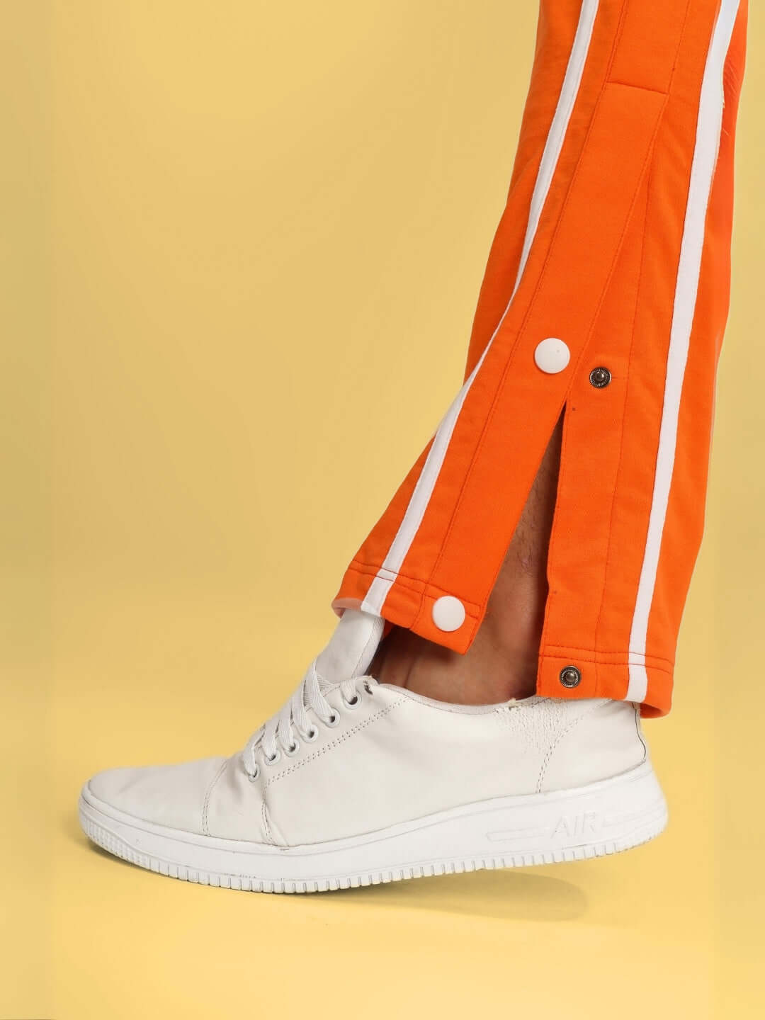 Model wearing orange contrast panel jogger pants with white sneakers on a yellow background.