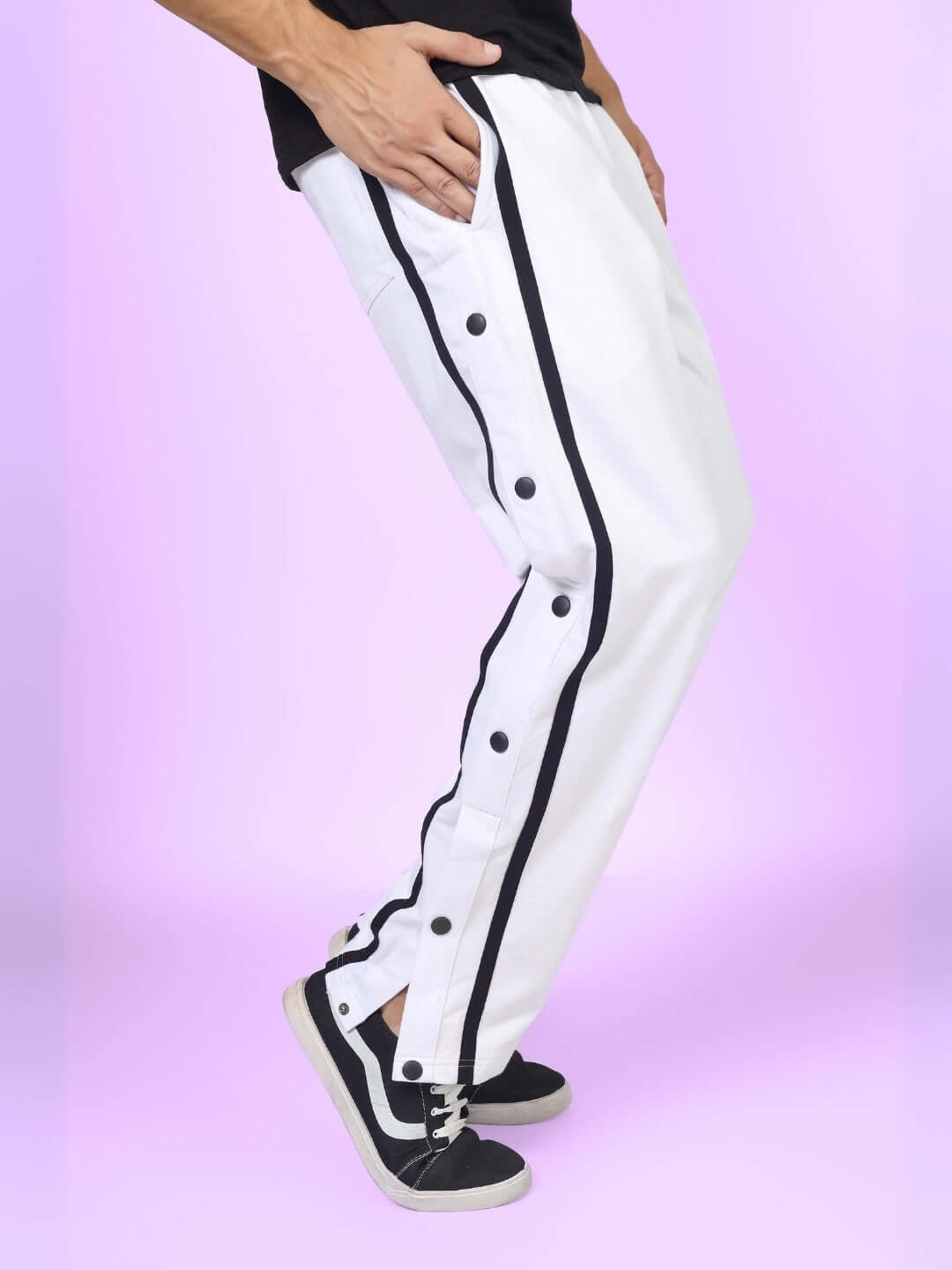 White joggers with contrast panels and button details, styled with black sneakers on a purple background.