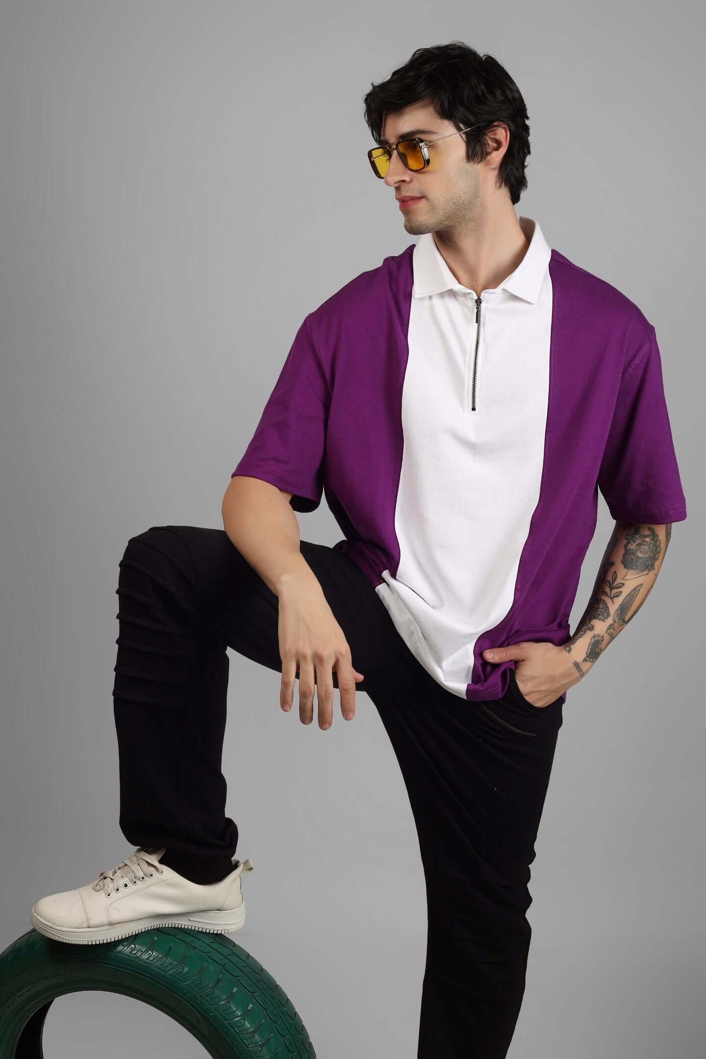 Model wearing oversized purple-white contrast polo t-shirt with zipper, heavy gauge cotton fabric, posing with yellow sunglasses and tattoo visible.