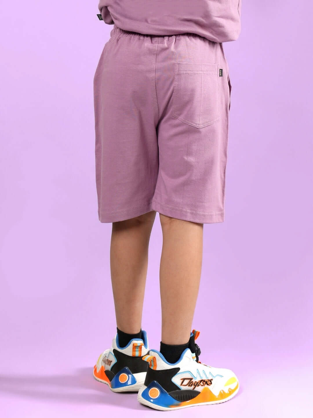 Child wearing COOKIE MONSTER PRINTED SHORTS FOR BOYS & GIRLS PLUM PURPLE, showcasing back view.