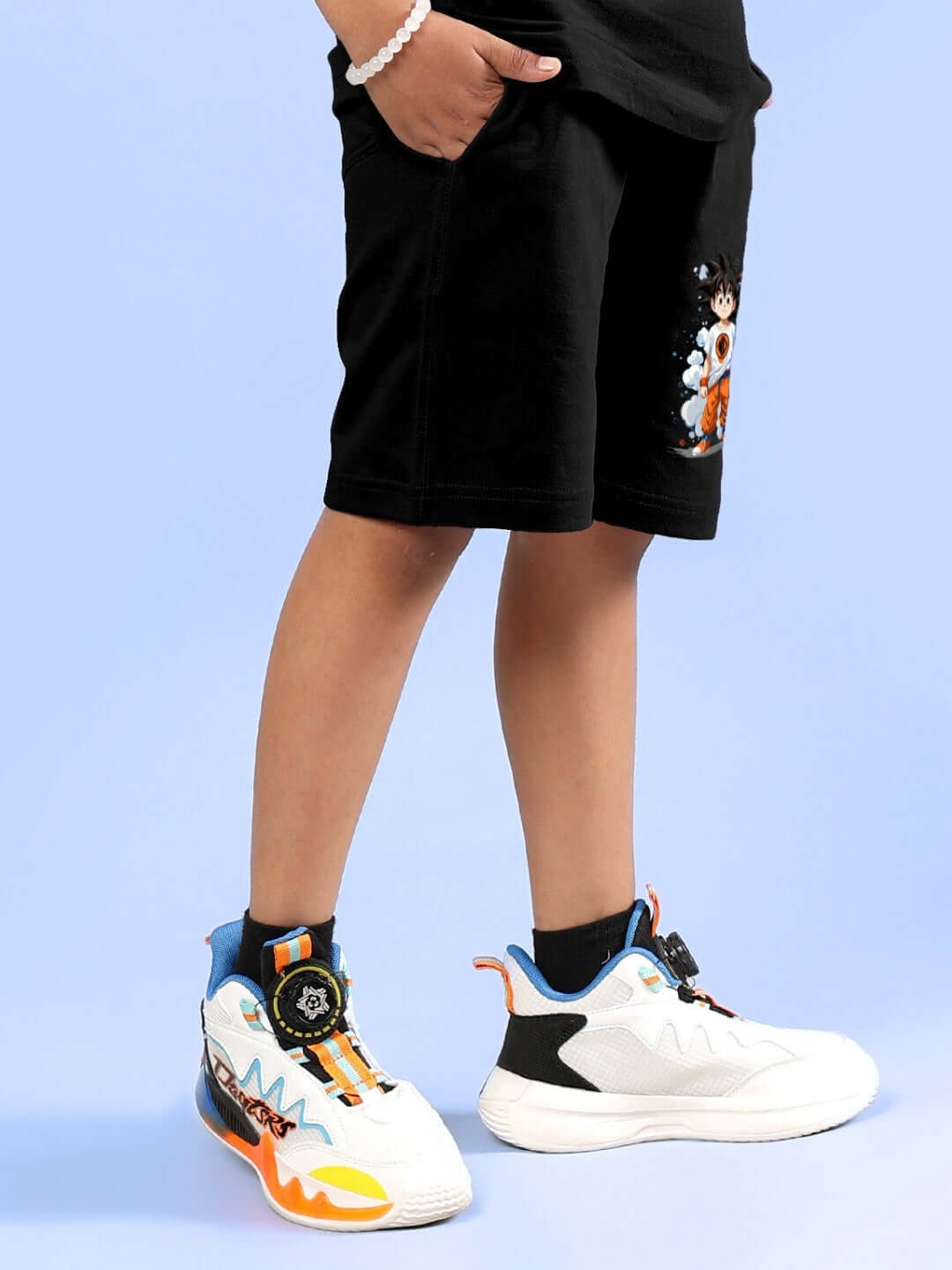 Child wearing black shorts with Goku print from DUDS, paired with colorful sneakers, featuring customizable size options.