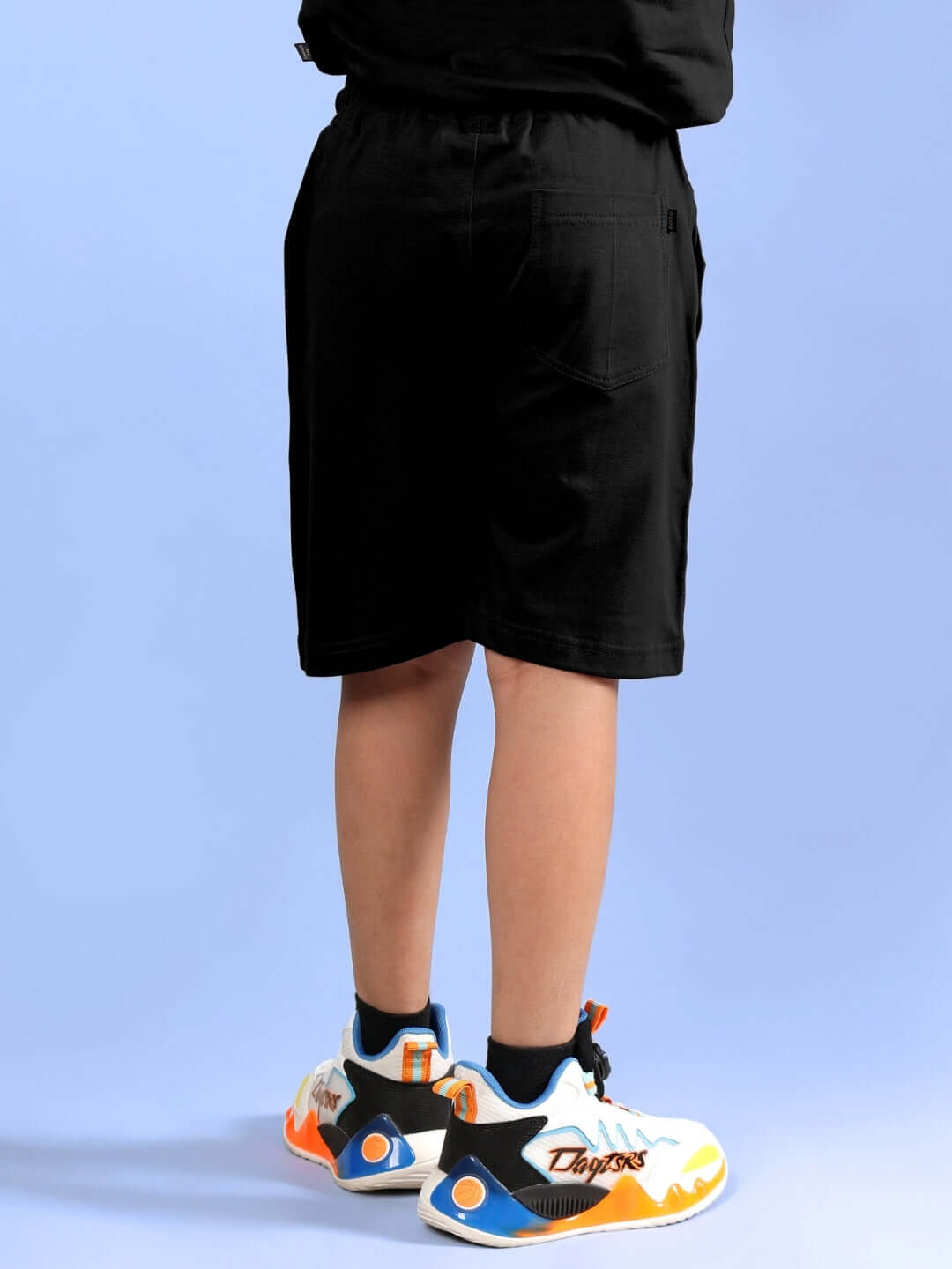 Cool Goku printed black shorts for boys and girls, rear view, paired with colorful sneakers.
