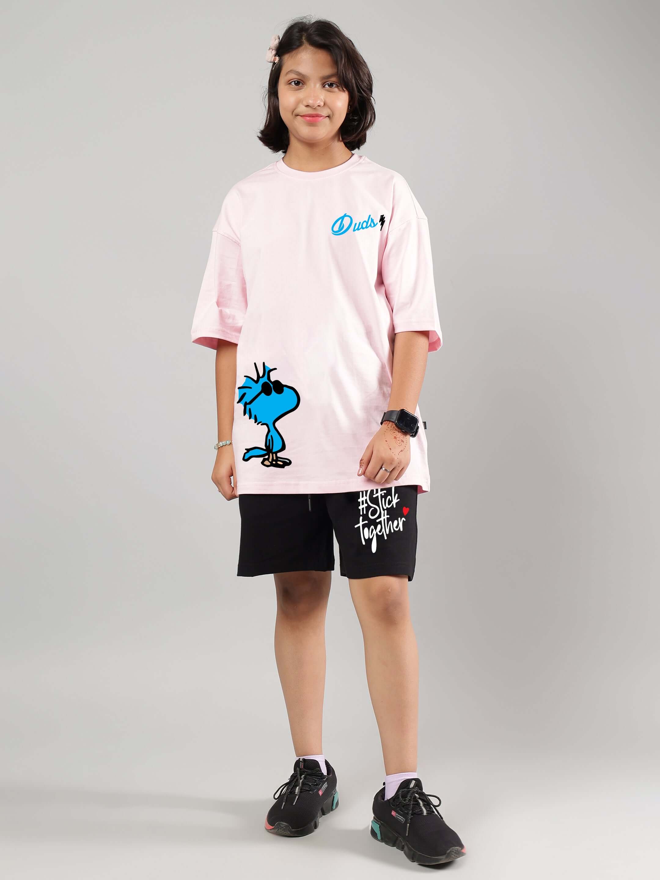 Child wearing COOL PALS pink-black co-ord set, featuring a pink t-shirt with cartoon graphic and black shorts with text detail.