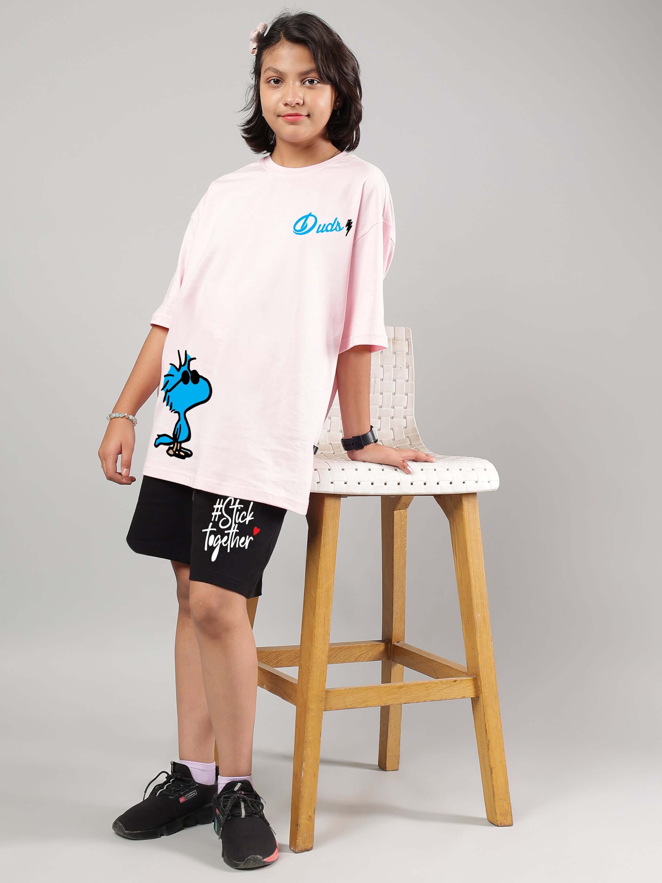 Child wearing COOL PALS CO-ORD FOR BOYS GIRLS PINK-BLACK, featuring pink t-shirt and black shorts, standing beside a chair.