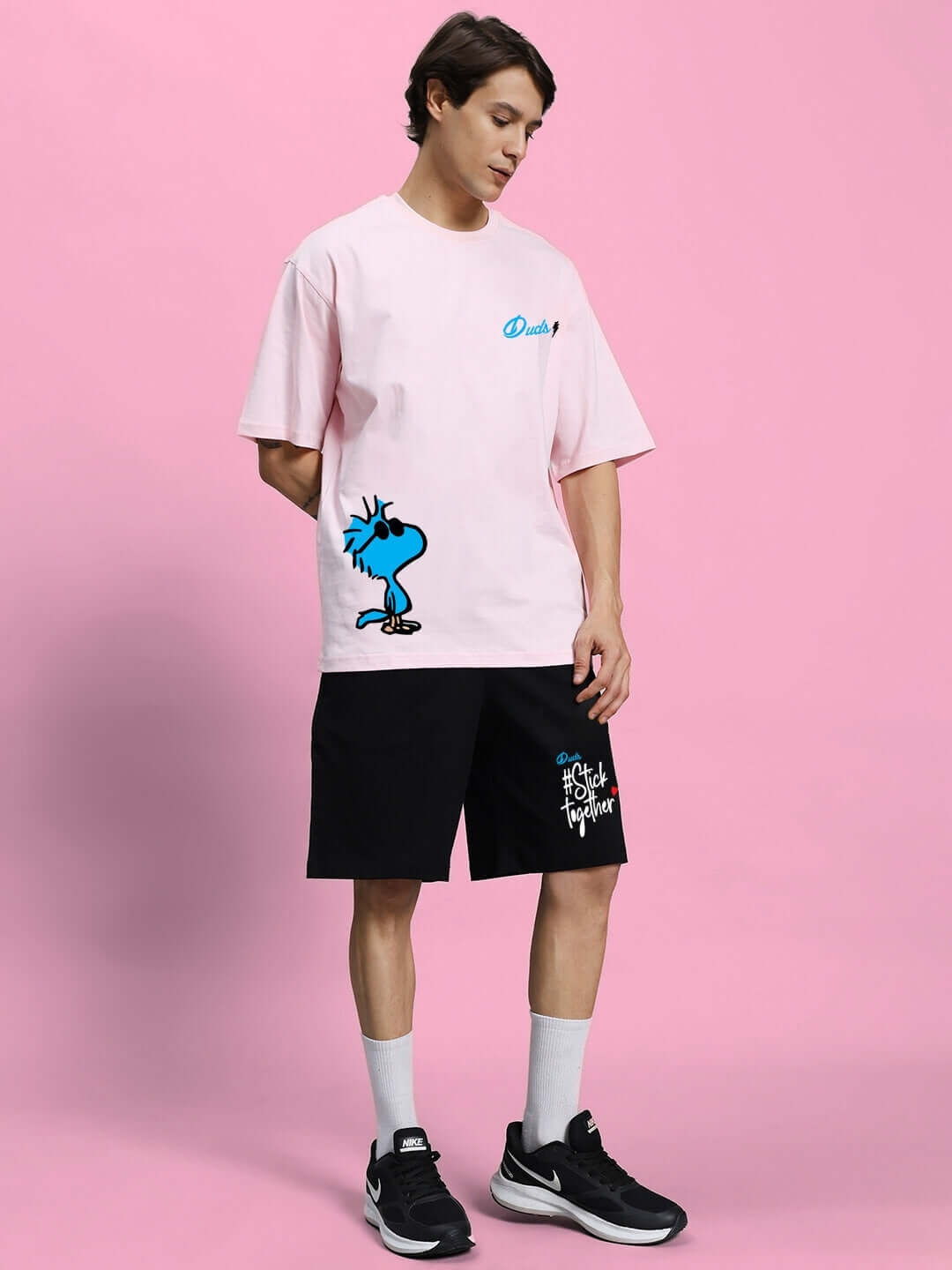 Model wearing COOL PALS SUMMER CO-ORD SET PINK BLACK with pink oversized t-shirt and black shorts on a pink background.