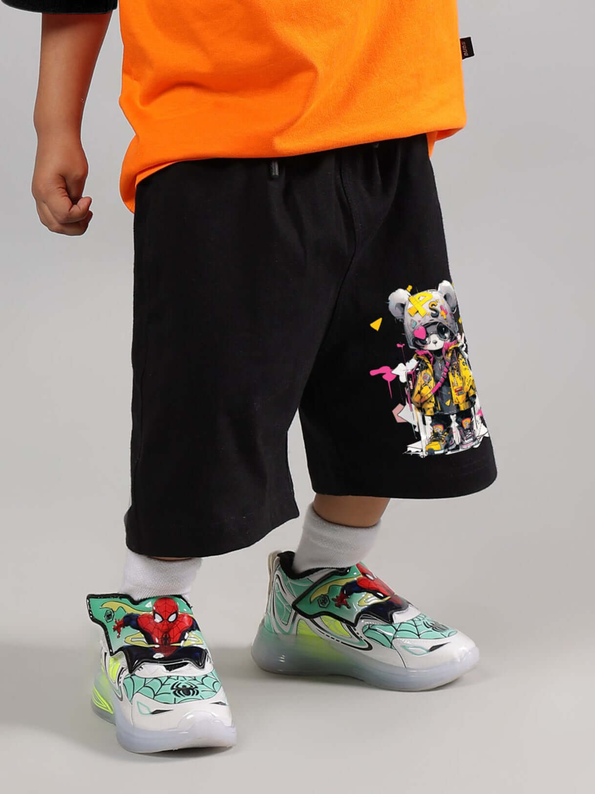 Child wearing COOL TEDDY SHORTS in black, featuring a colorful teddy design, paired with vibrant shoes, ideal for both boys & girls.