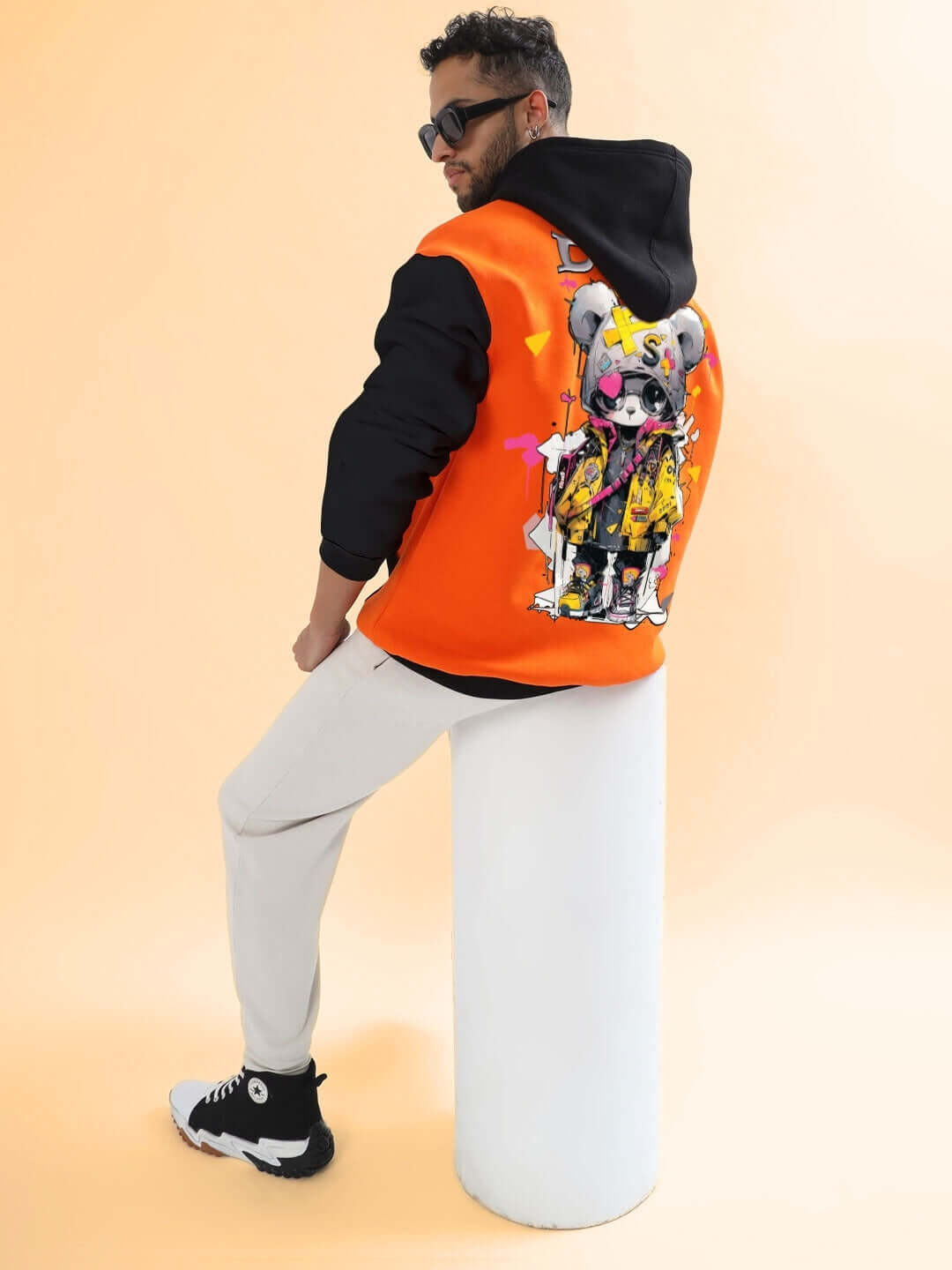 Man wearing COOL TEDDY FLEECE COLORBLOCK OVERSIZE HOODIE ORANGE BLACK with graphic design, sitting on a white stool.