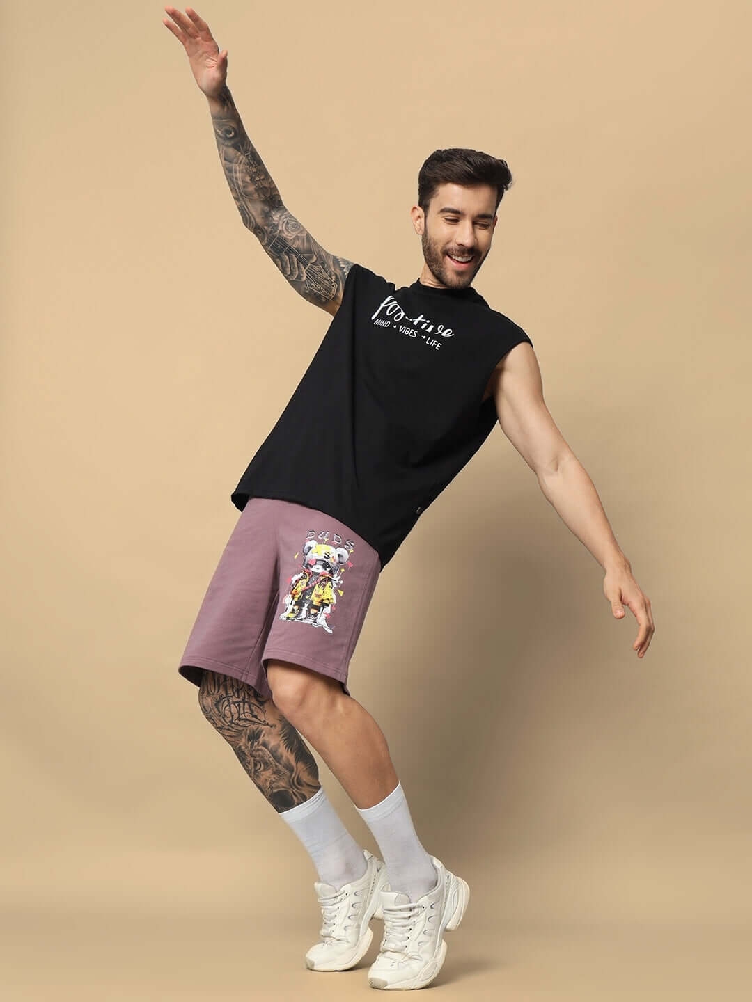 Man wearing COOL TEDDY regular fit shorts in Chinese violet, dancing energetically, paired with a black sleeveless shirt and white sneakers.