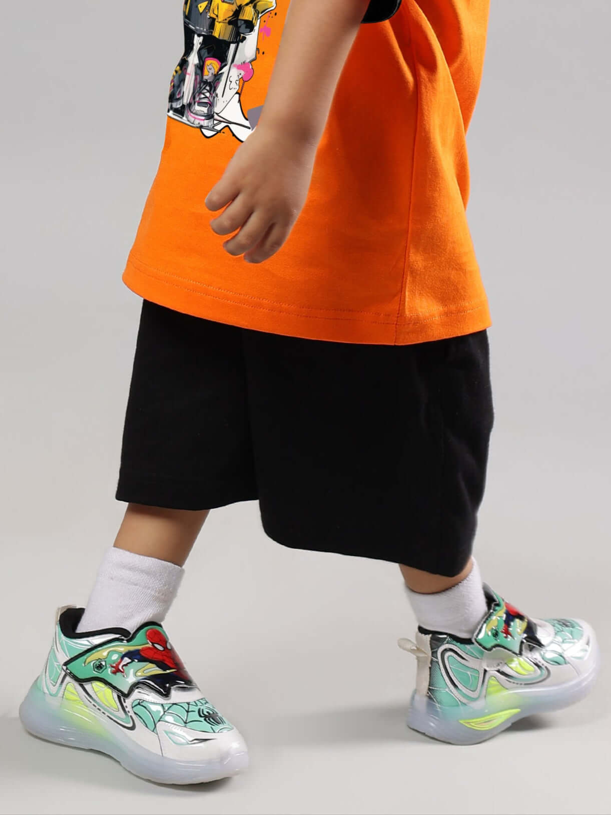 Child wearing black COOL TEDDY SHORTS for boys and girls paired with colorful sneakers and an orange shirt.