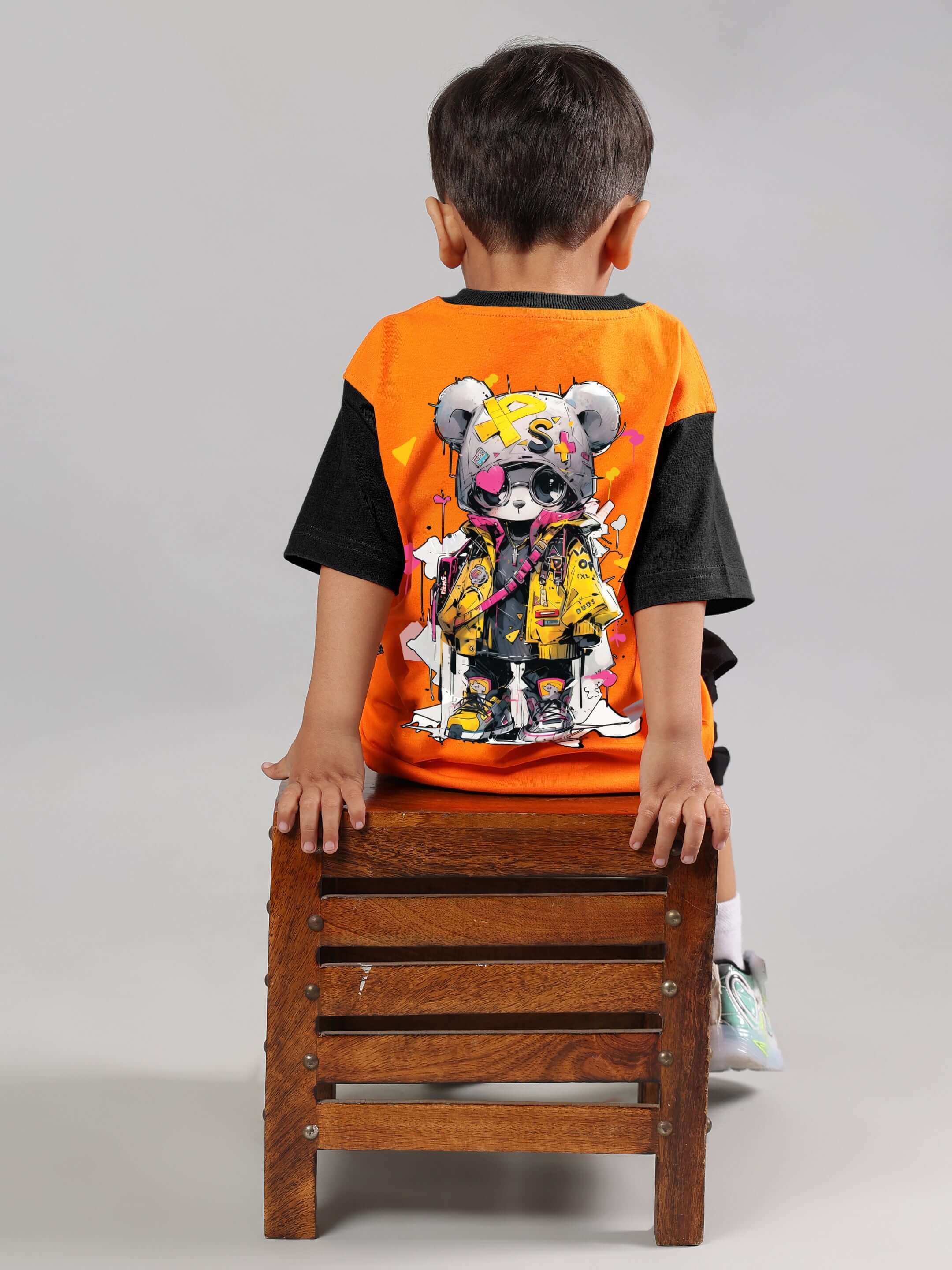 Child wearing orange Cool Teddy T-shirt for boys and girls, sitting on a wooden stool. Made to order by DUDS.