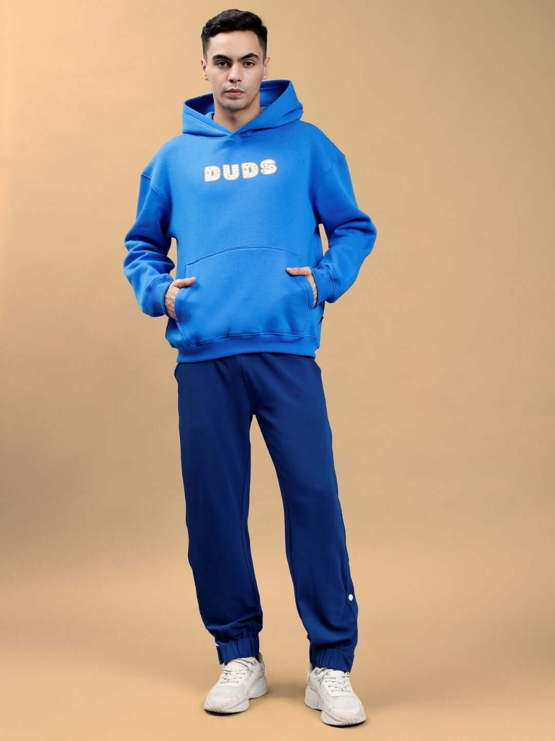 Man in a royal blue oversized hoodie with 'COURAGE' text, standing against a neutral background, showcasing trendy casual wear fashion.