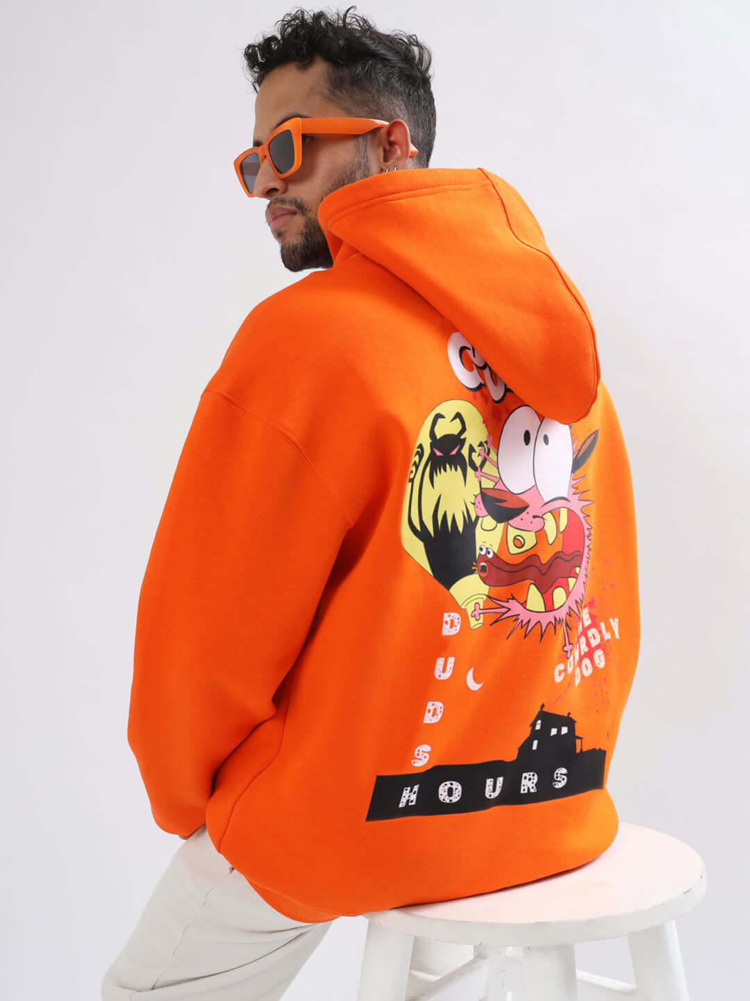 Orange oversized hoodie with cartoon graphic on the back, worn by a person sitting, showcasing the Courage design, custom fit available.