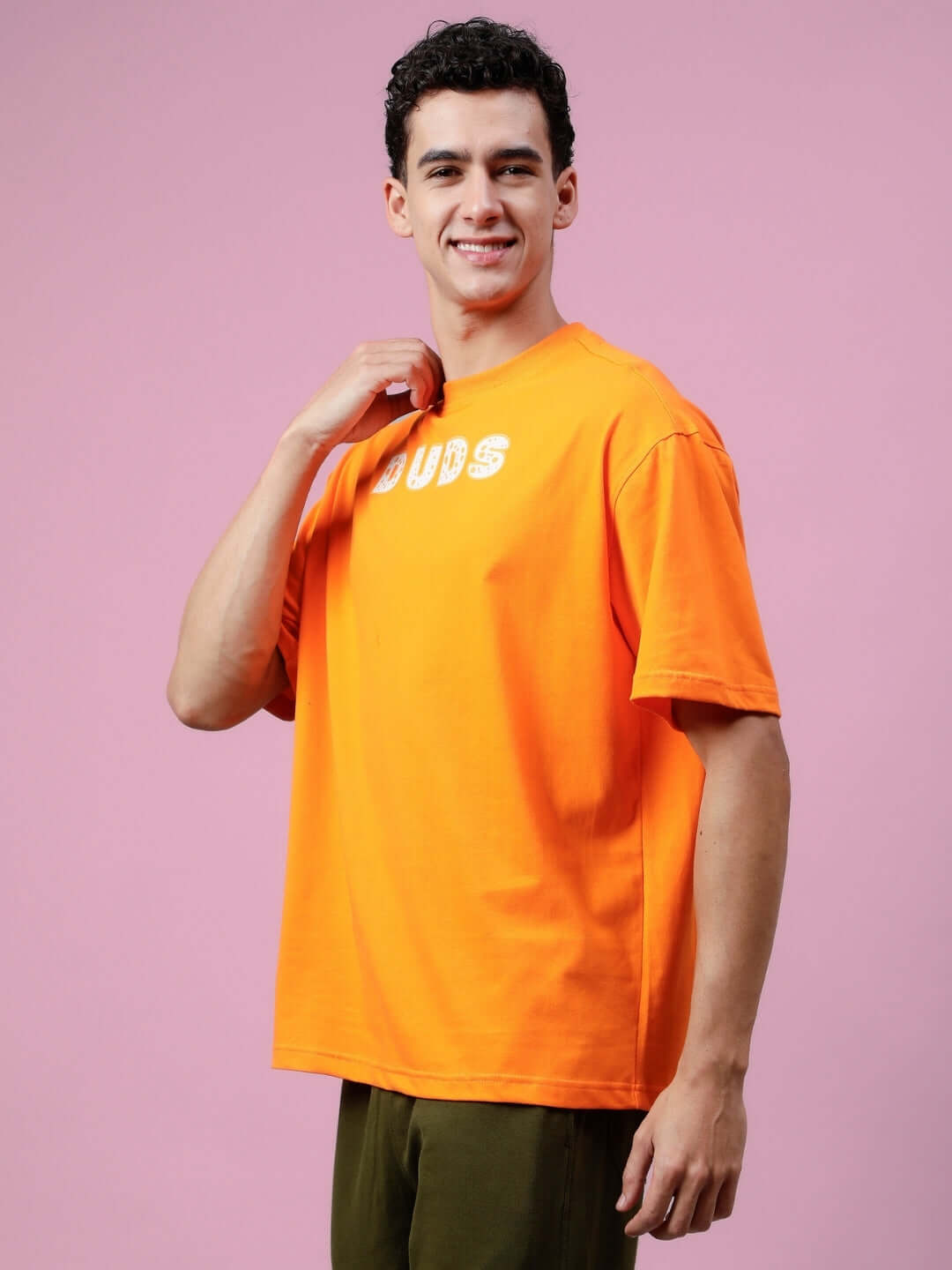 Model wearing Courage oversized orange t-shirt by DUDS with custom fit option for personalized size. Casual fashion on pink background.