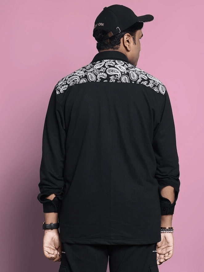 Back view of a man wearing a black COVE SHIRT by DUDS, featuring detailed patterns on the upper back, against a pink background.