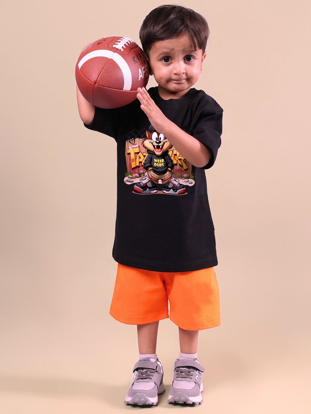 Child wearing Crazy Rapper co-ord outfit in black and orange, holding a football, showcasing hip-hop style for kids