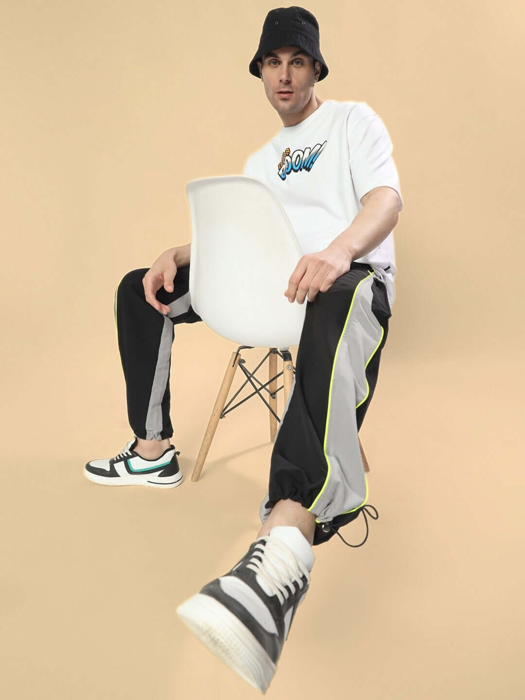 Model wearing CRAZY RELAXED FIT CARGO PANTS in black-grey, sitting on a chair, showcasing casual style.