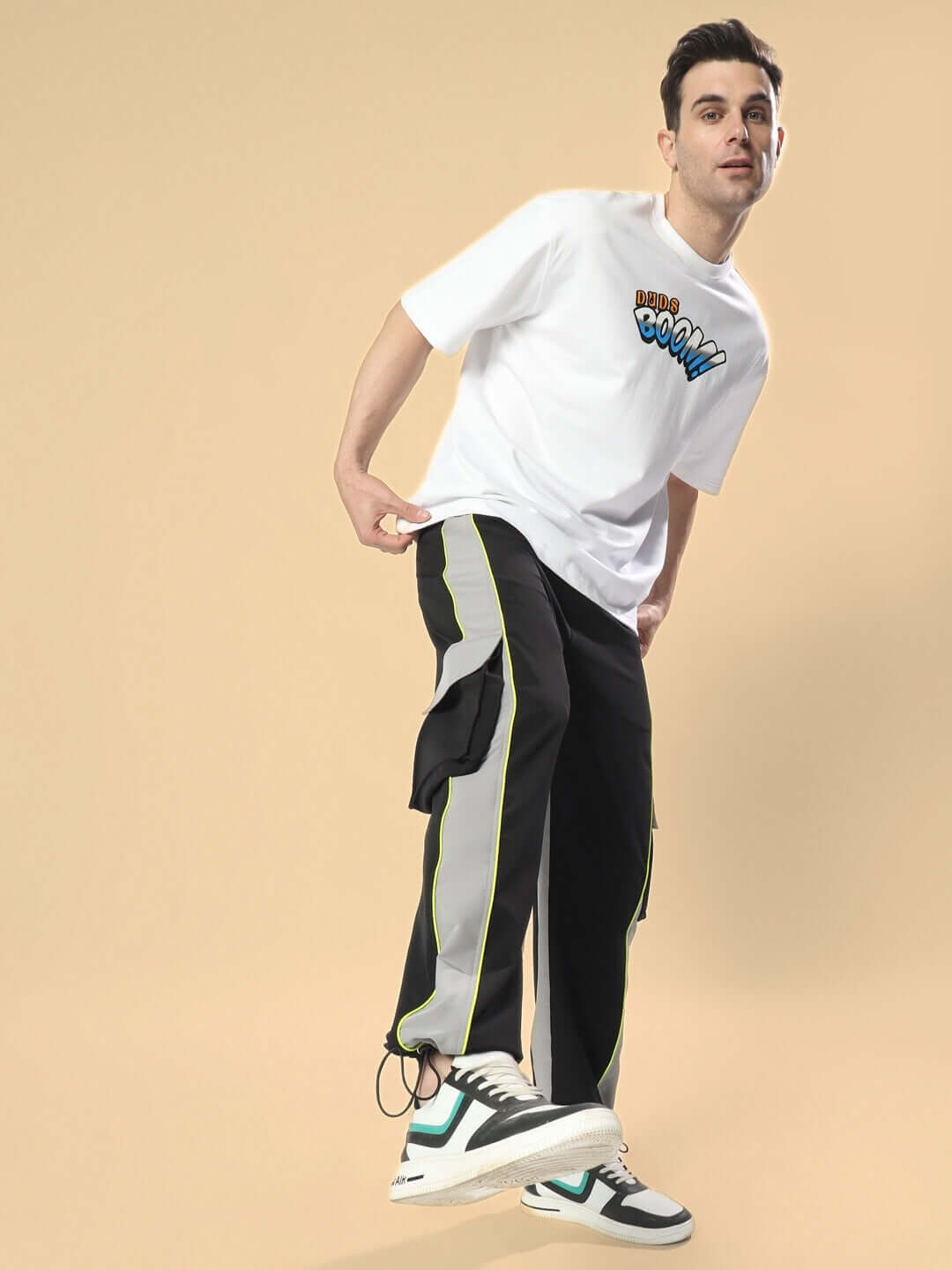 Model wearing black-grey cargo pants with relaxed fit, paired with graphic tee and sneakers on beige background.
