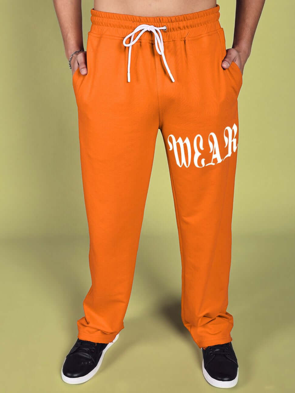 Orange relaxed fit jogger pants with drawstring, featuring white lettering on the leg, styled with black sneakers.