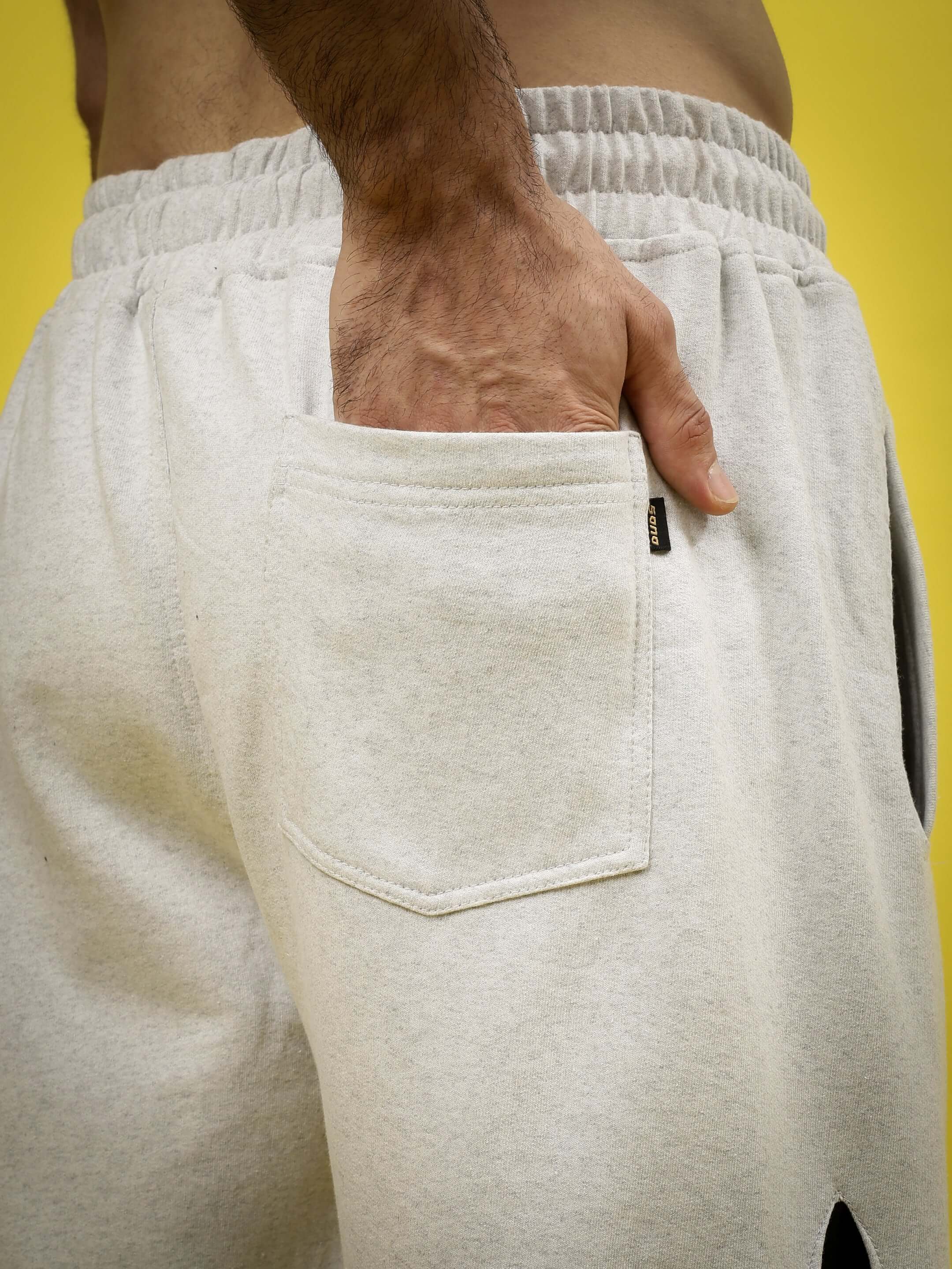 Close-up of light grey jogger pants with a hand in the pocket, featuring a crossed star design. Perfect for custom fit orders.