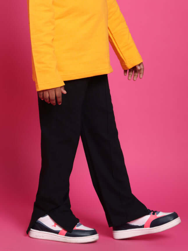 Child wearing DUDS CUBE Jogger for Boys & Girls in black, paired with colorful sneakers and a vibrant pink backdrop.