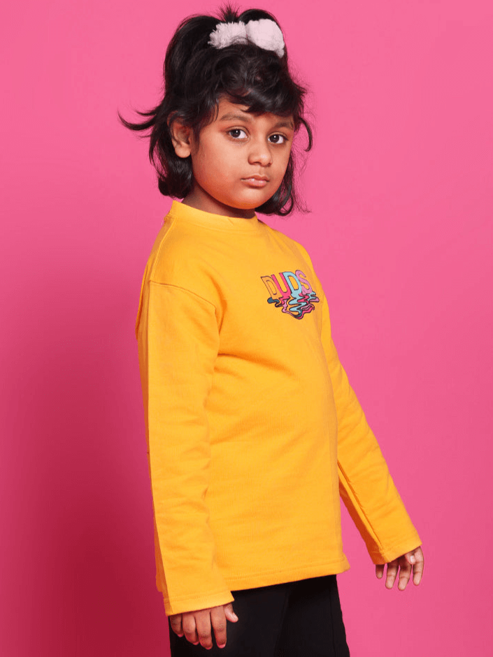 Child wearing a yellow DUDS oversized sweatshirt, standing against a pink background, showcasing the vibrant and comfortable design.