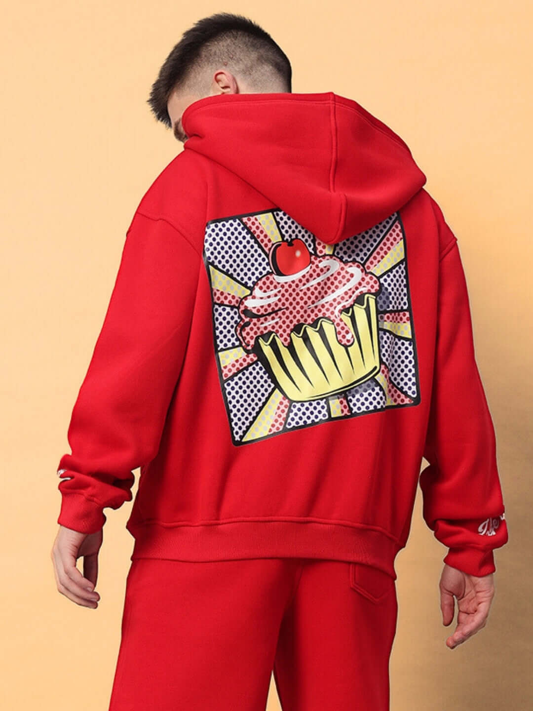 Person wearing CUPCAKE COTTON FLEECE HOODIE RED with bold cupcake graphic on the back, showcasing vibrant streetwear style.