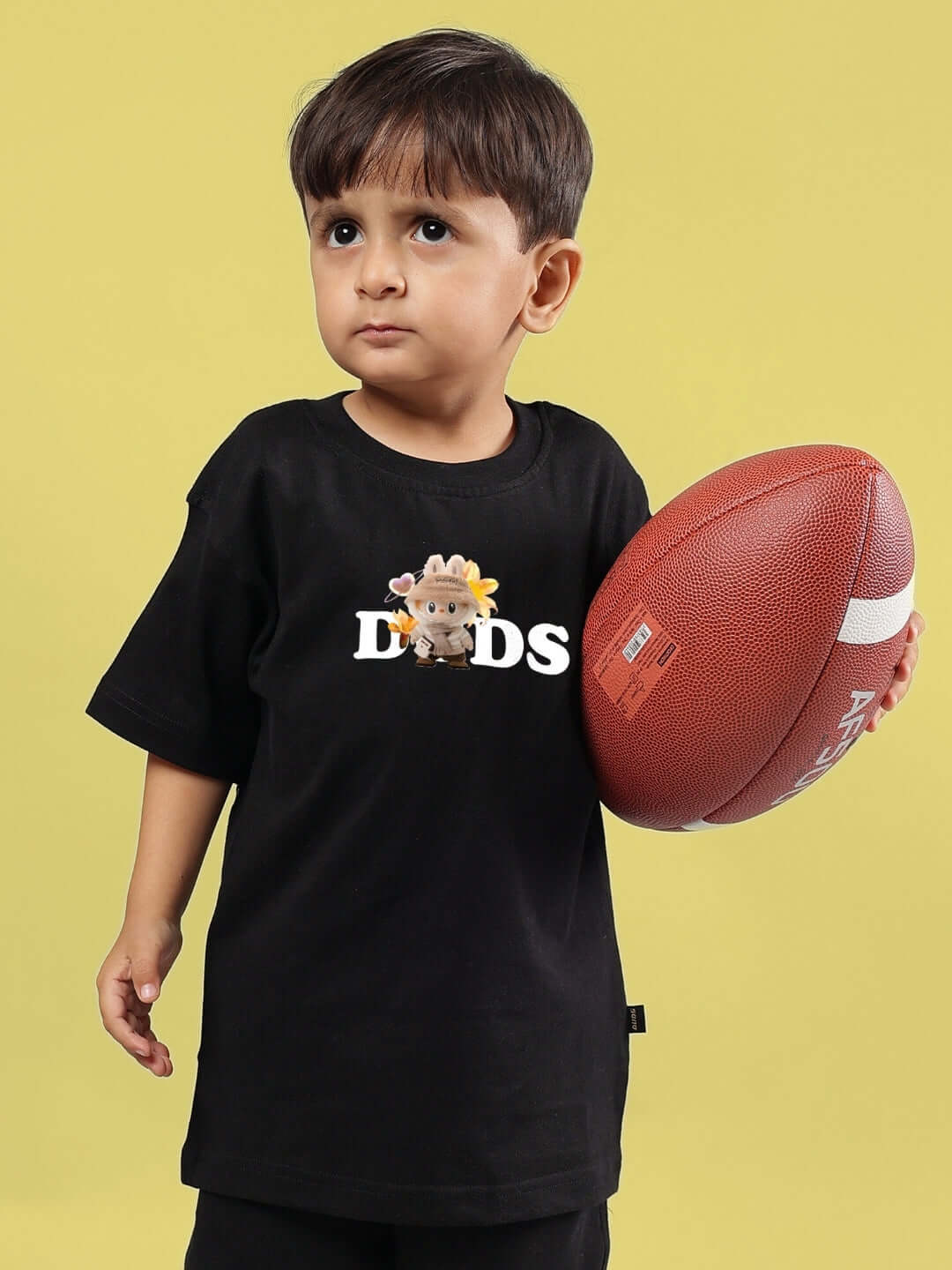 Child wearing a black Cute Monsters T-shirt for boys and girls, holding a football, by DUDS.