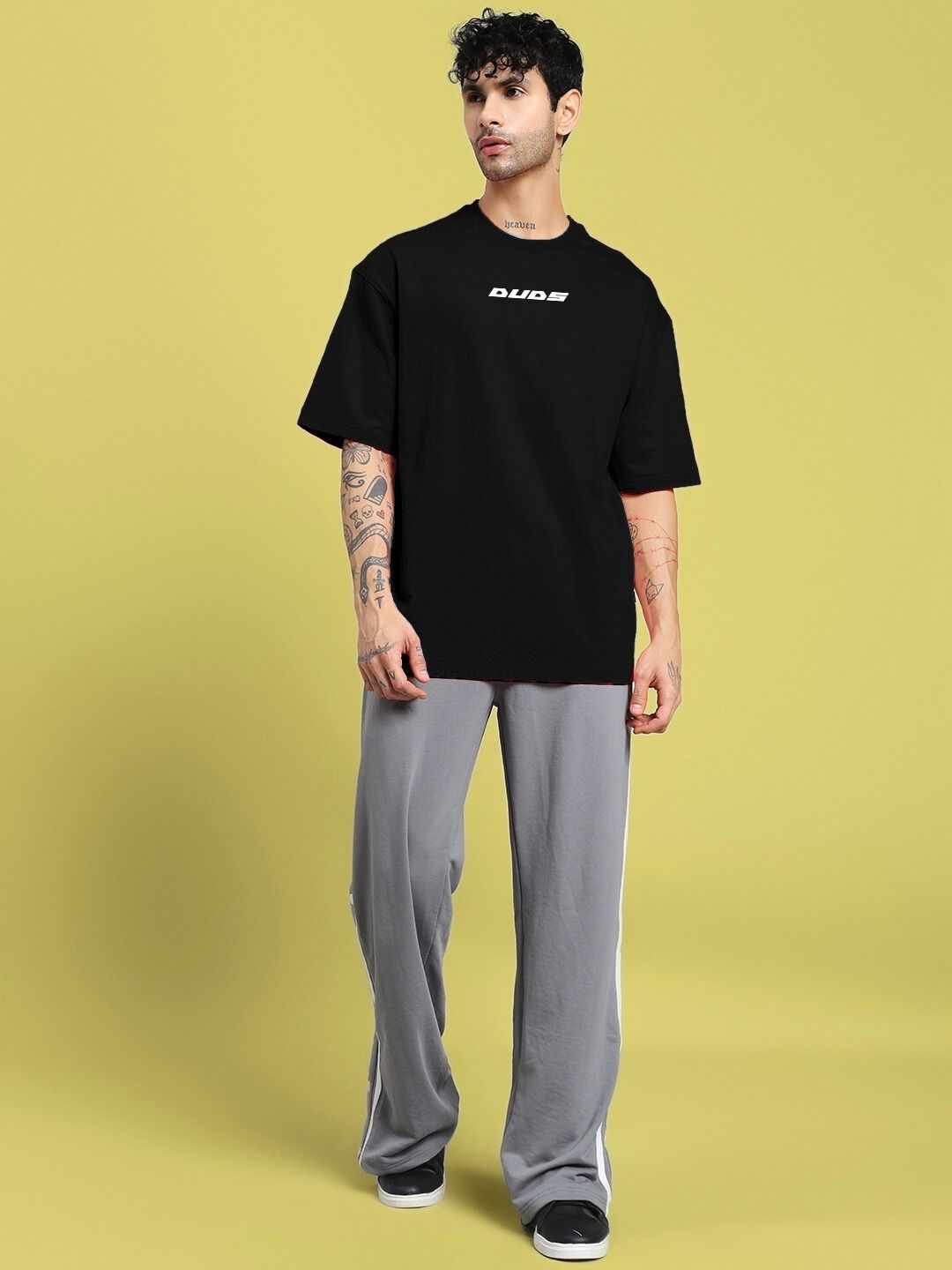 Man wearing CYBERPUNK OVER-SIZED T-SHIRT BLACK, showcasing futuristic street style with graphic detailing on a yellow background.