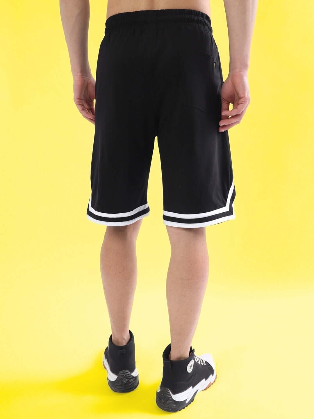 Back view of black regular fit shorts with white trim, perfect for custom fitting options, showcased against a yellow background.