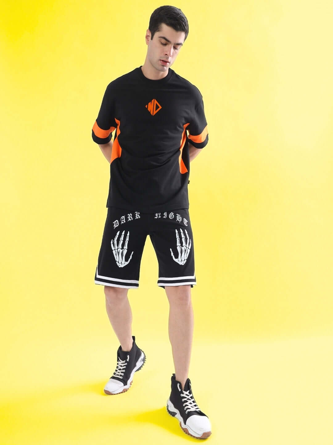 DARK NIGHT regular fit black shorts with white skeleton design, modeled with sneakers and casual top on yellow background.