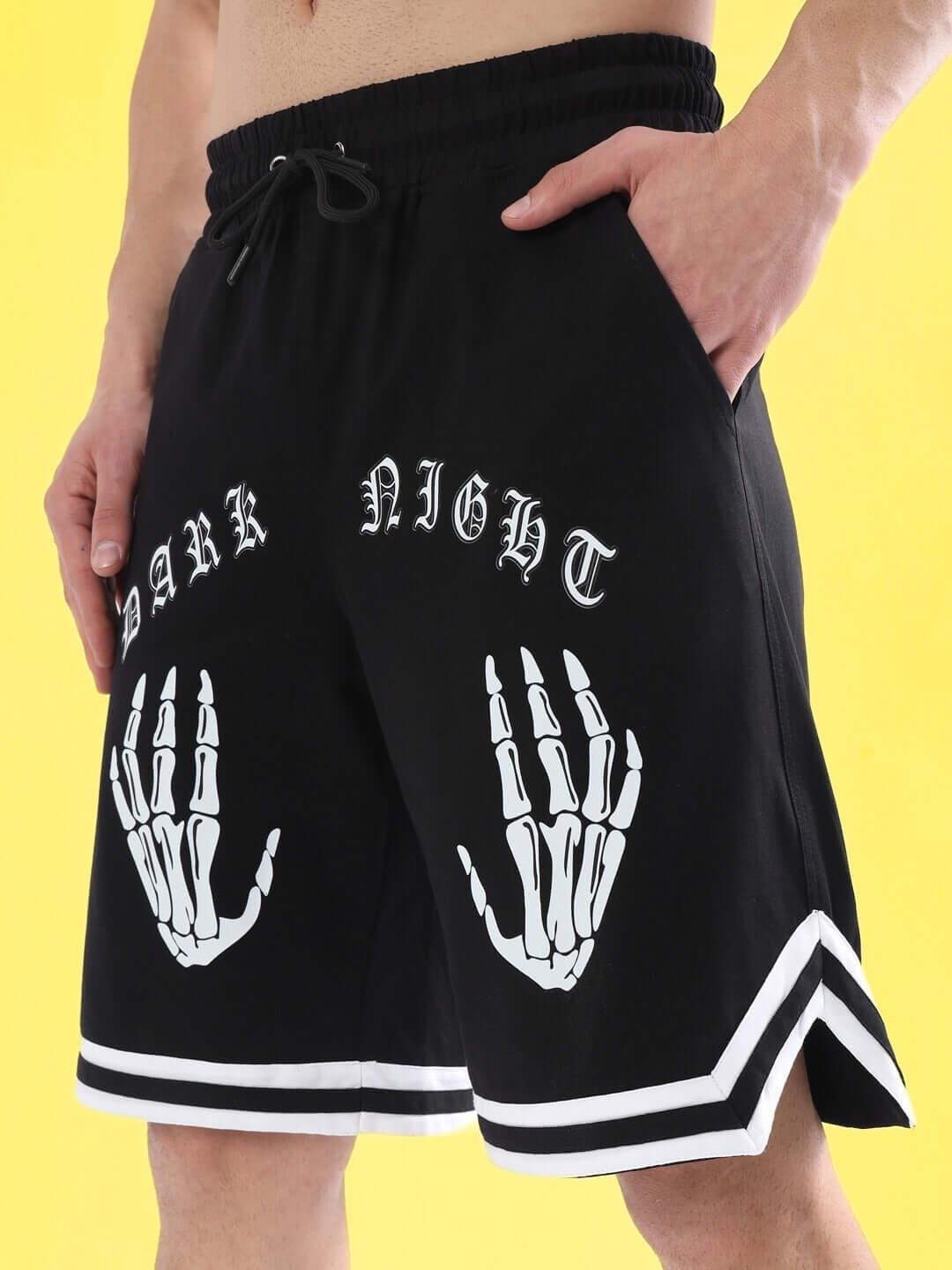 Person wearing black Dark Night shorts with skeleton hand design and text, featuring a comfortable drawstring waist and regular fit.