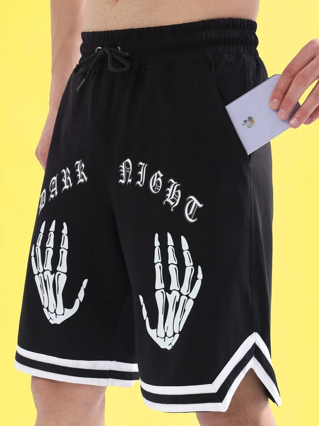 Man wearing black Dark Night shorts with skeleton print, holding a phone in the pocket.