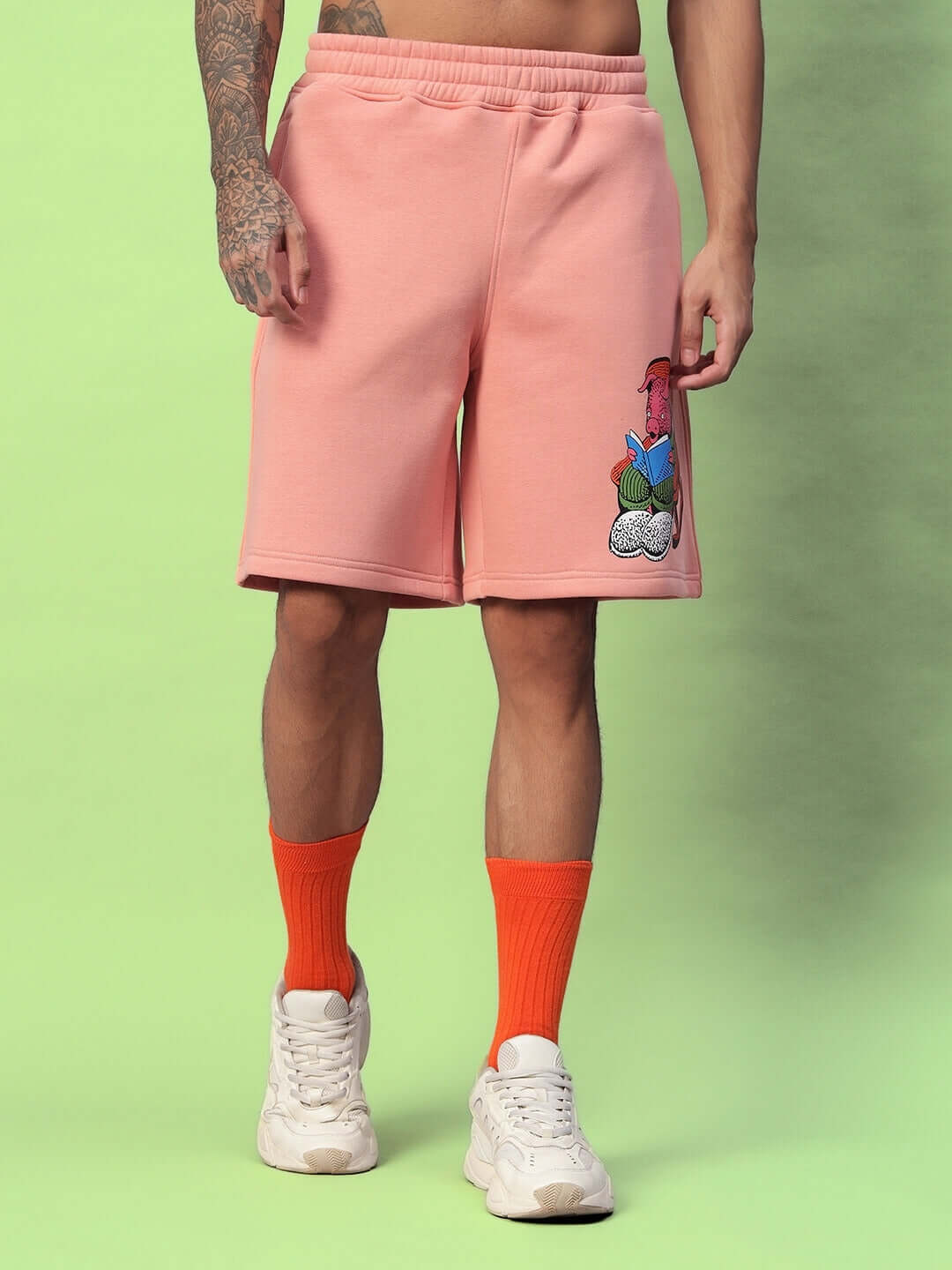 Person wearing DELIBERATE FLEECE SHORTS PEACH with orange socks and white shoes on a green background.