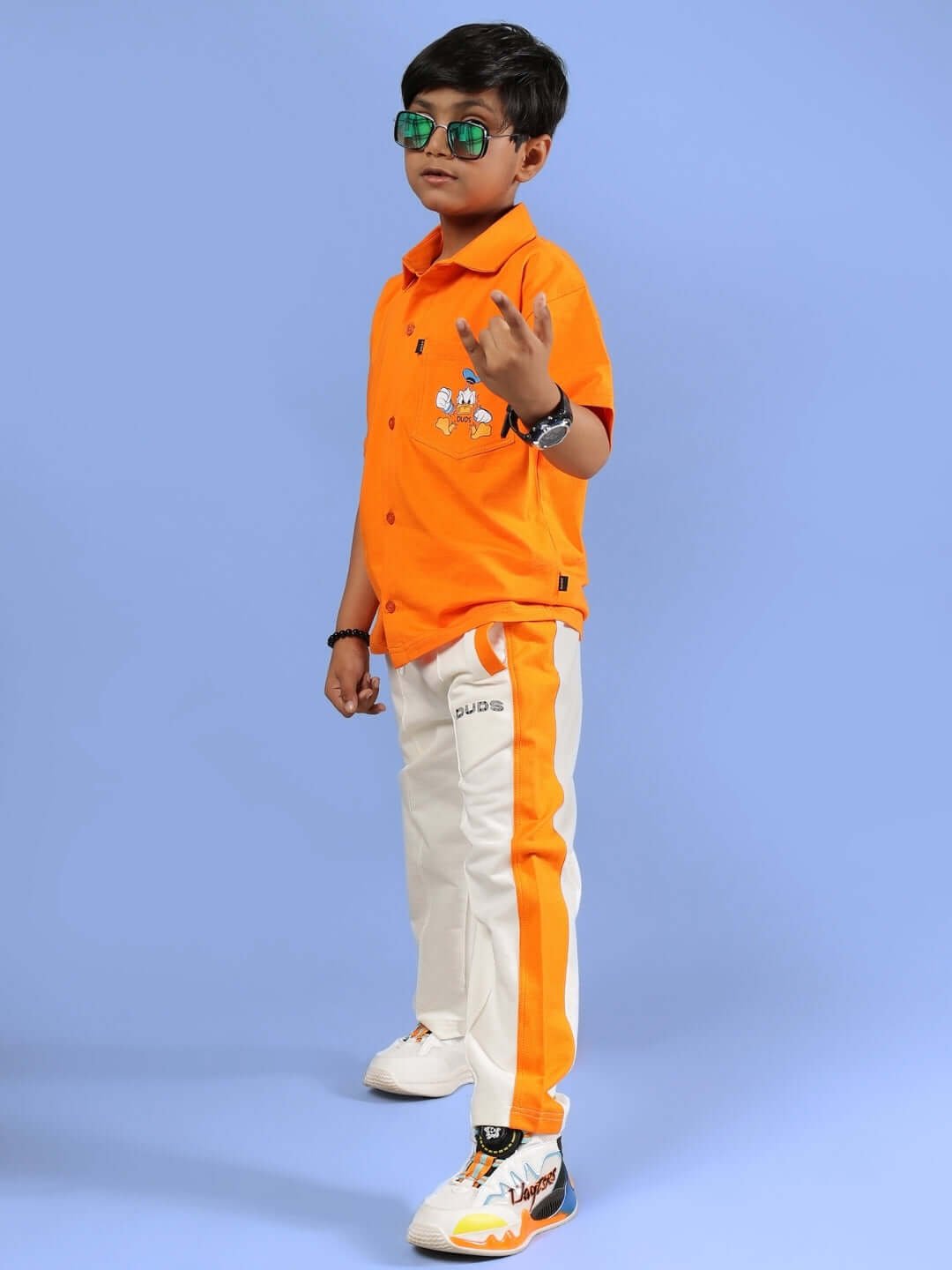 Child wearing DELLA CO-ORD FOR BOYS & GIRLS ORANGE outfit with vibrant design, perfect for play and style, against a blue background.