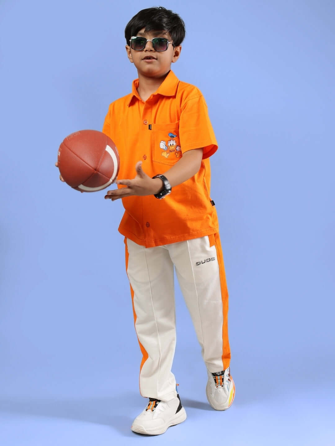 Boy wearing Della Co-ord in orange by DUDS, holding a football, showcasing customizable made-to-order clothing for kids.
