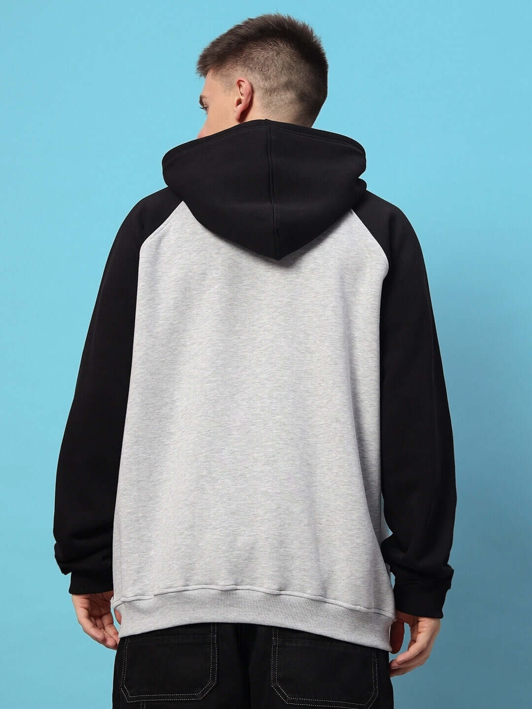 Back view of DELUXE FLEECE COLORBLOCK OVERSIZE HOODIE BLACK MELANGE GREY worn by model against blue background