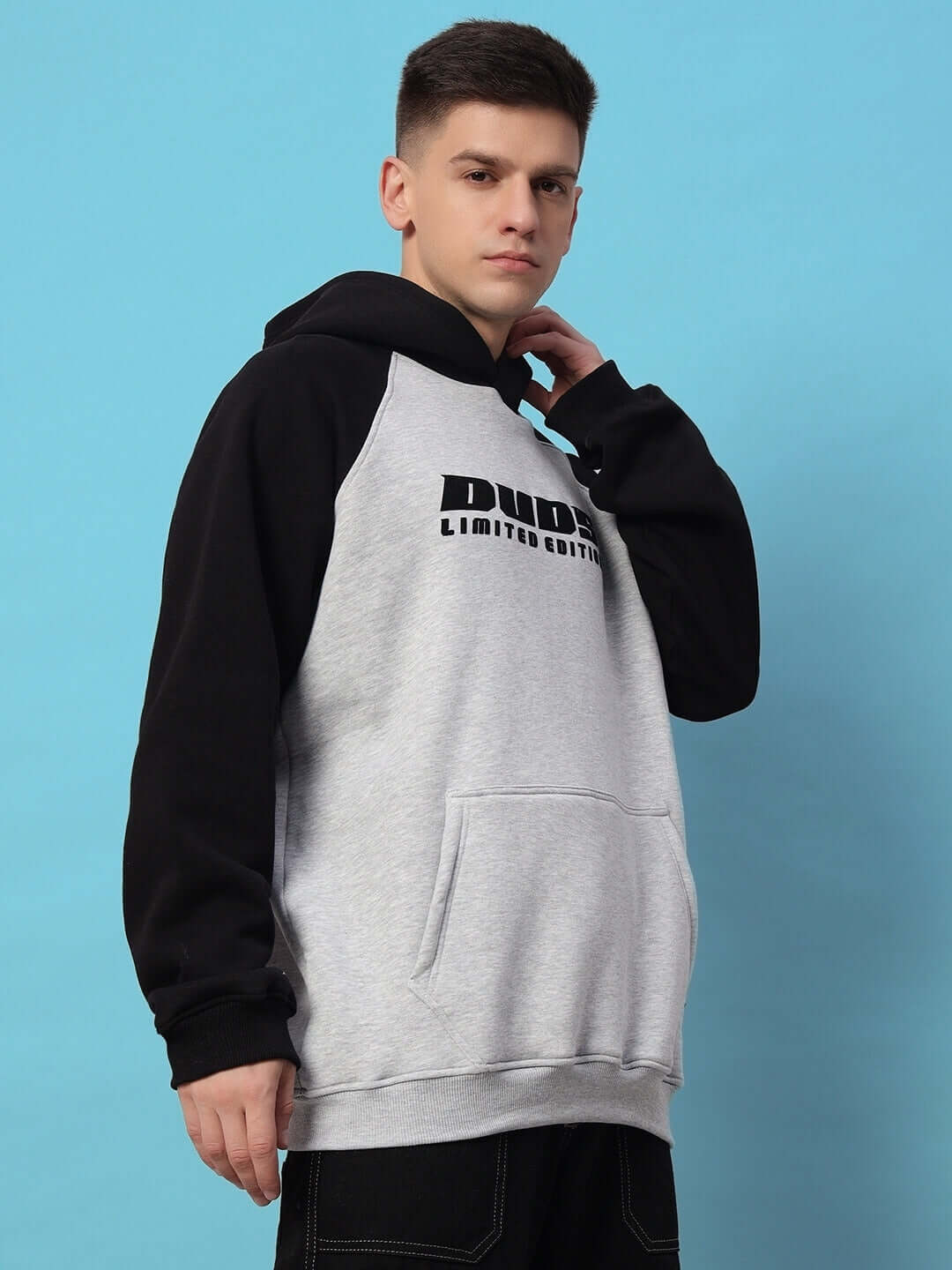 Man wearing DELUXE FLEECE COLORBLOCK OVERSIZE HOODIE BLACK MELANGE GREY, showcasing urban streetwear with modern design.
