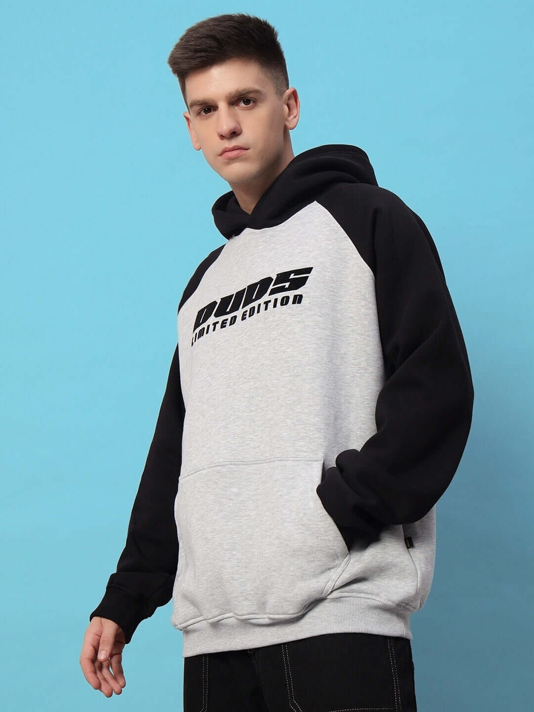 DELUXE FLEECE COLORBLOCK OVERSIZE HOODIE BLACK MELANGE GREY worn by a model against a blue background, showcasing casual streetwear style.