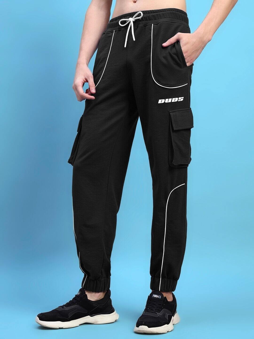 Alt Tag: Model wearing black DEVENO relaxed-fit joggers with DUDS logo, showcasing sporty design and comfort on a blue background.