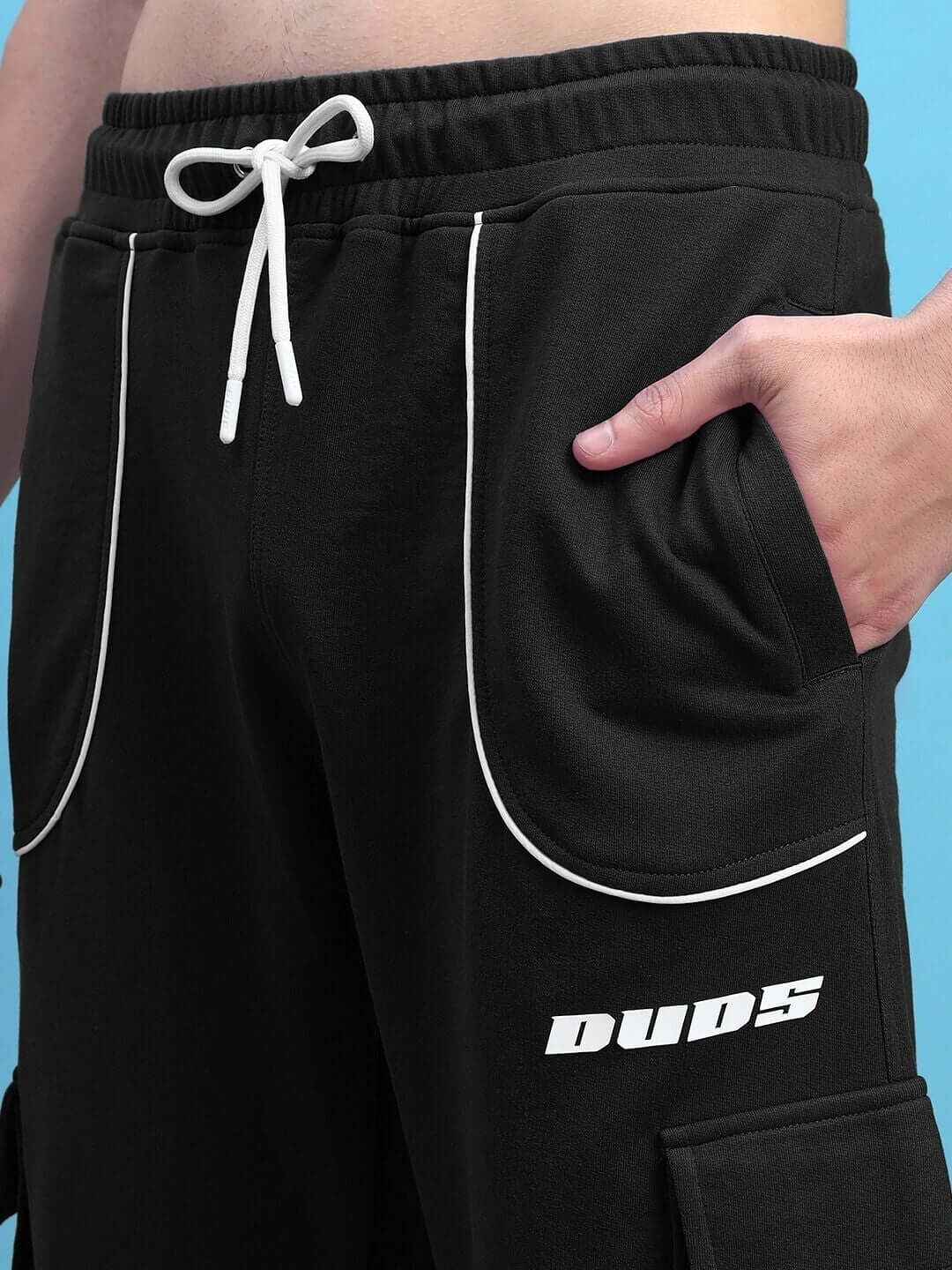 Close-up of DEVENO relaxed-fit black joggers with white drawstring, showing elegant design and DUDS logo.