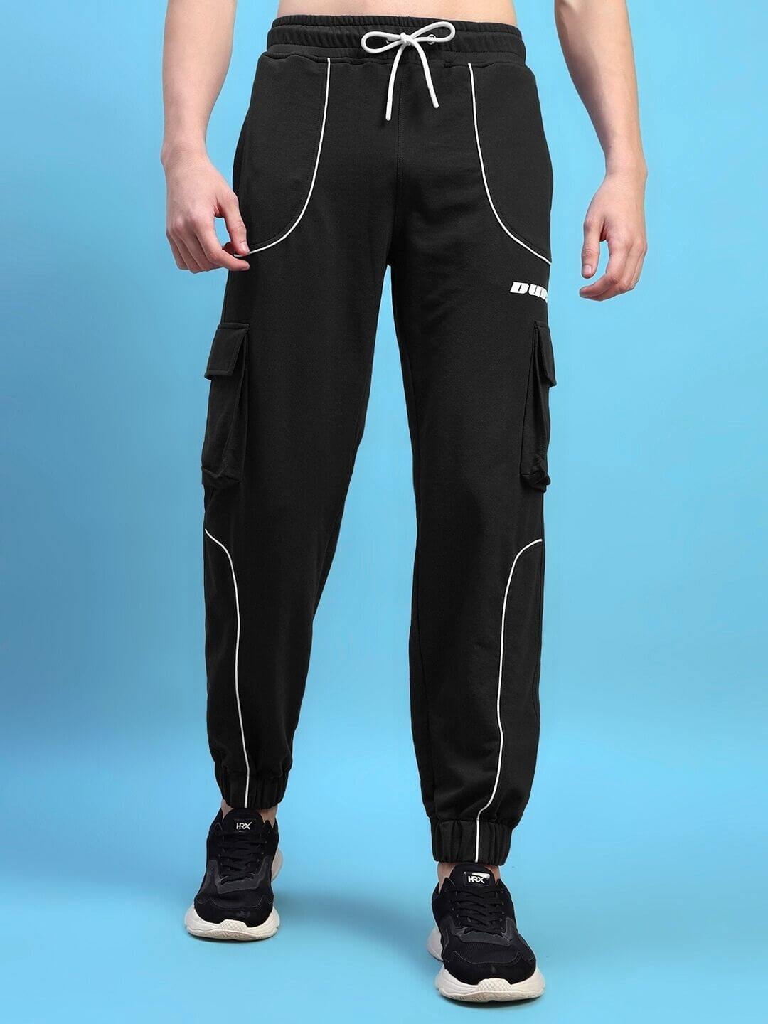 Man wearing Deveno relaxed-fit black joggers with white stitching and cargo pockets, standing against a blue background.