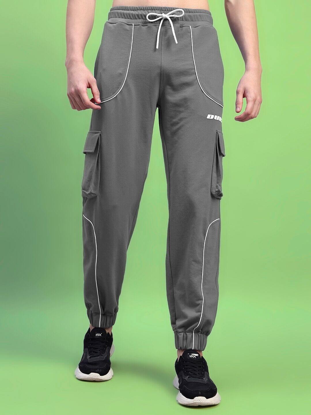Model wearing DEVENO Relaxed-Fit Grey Joggers with cargo pockets, featuring drawstring waist against a green background.
