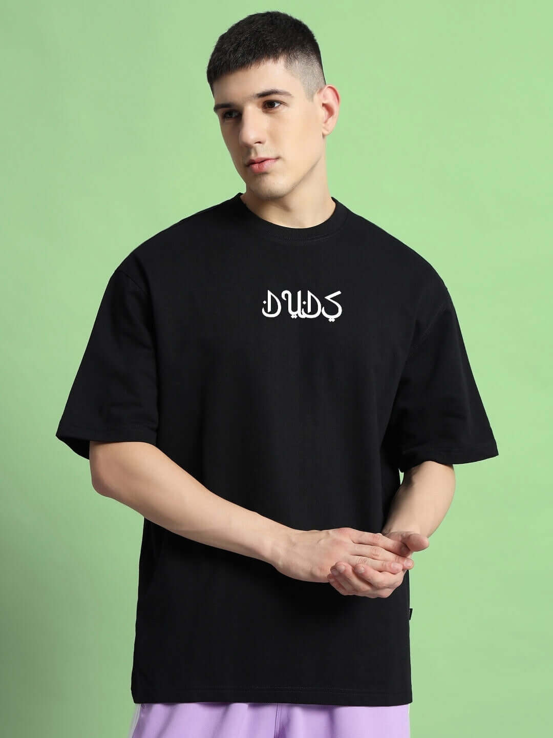 Model wearing Dimension Oversized Black T-Shirt made of 97% cotton and 3% elastane, on green background. Premium heavy gauge fabric.