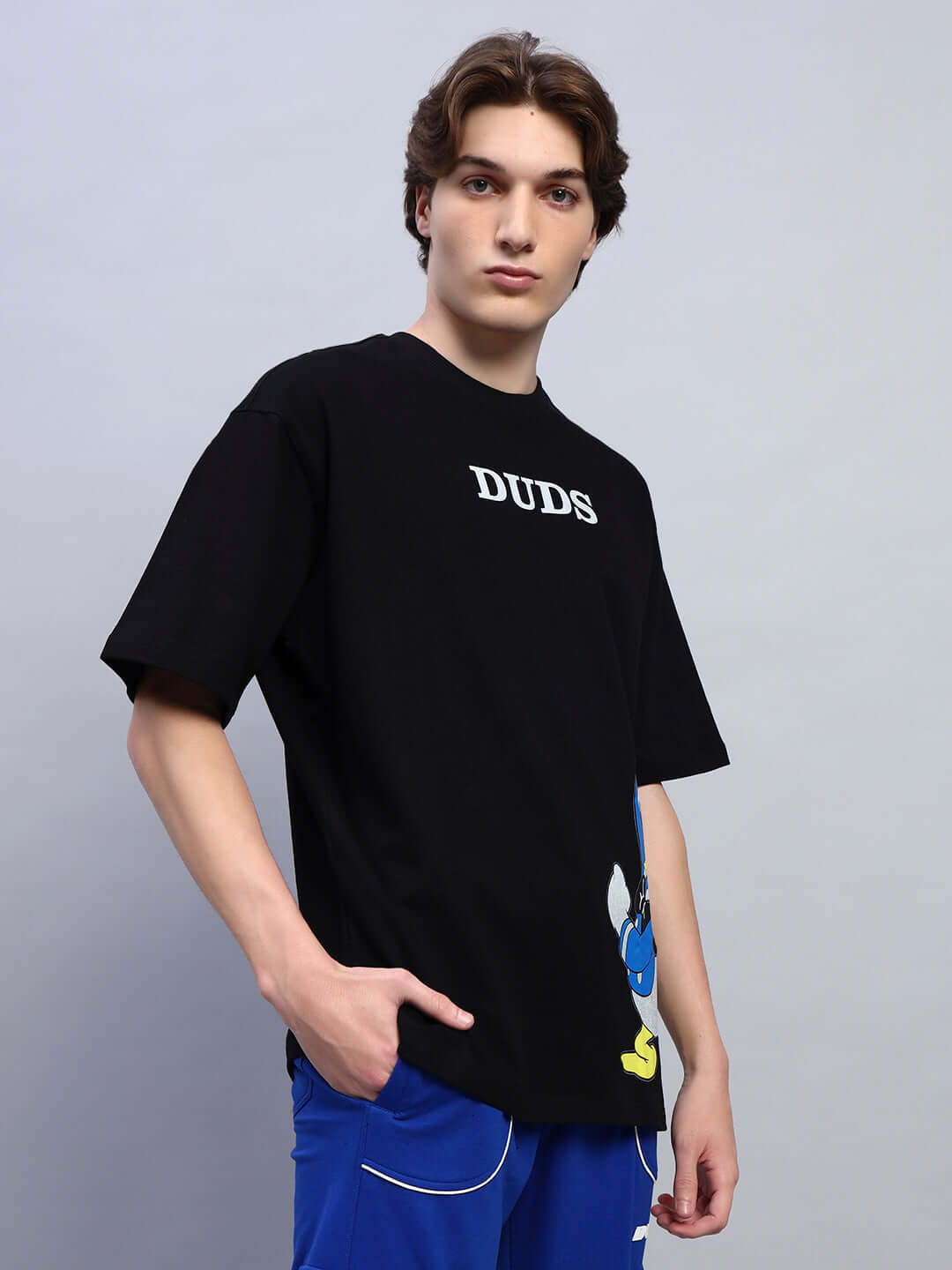Model wearing DONALD DUCK PRINTED OVERSIZED T-SHIRT BLACK with Donald Duck graphic on black base, showcasing modern streetwear style.